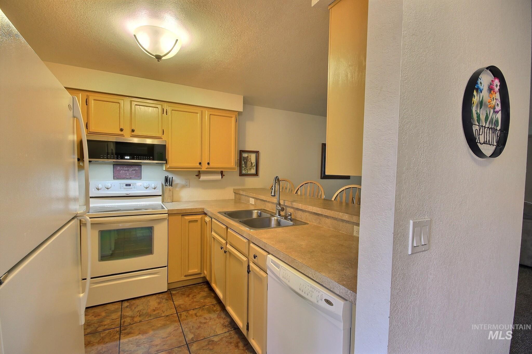 Kitchen with white appliances, light countertops, a textured ceiling, a peninsula, and a textured wall