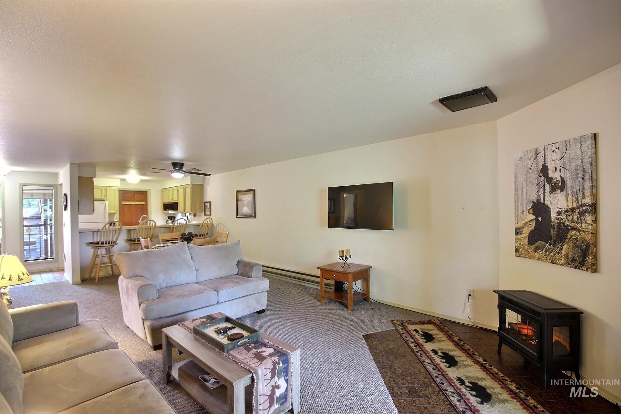 Living room with a wood stove, ceiling fan, a baseboard radiator, and carpet flooring