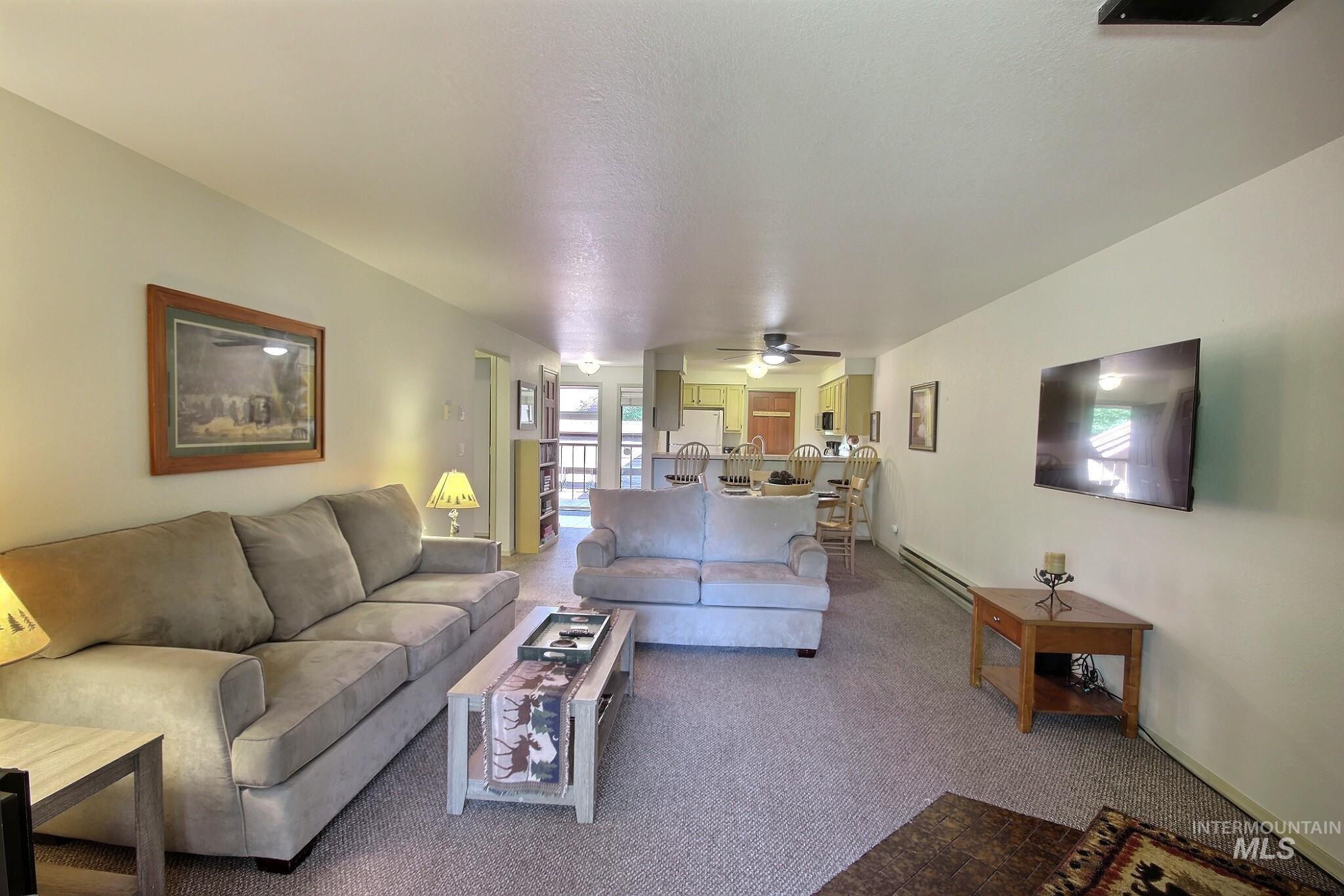 Carpeted living room with a baseboard heating unit and ceiling fan