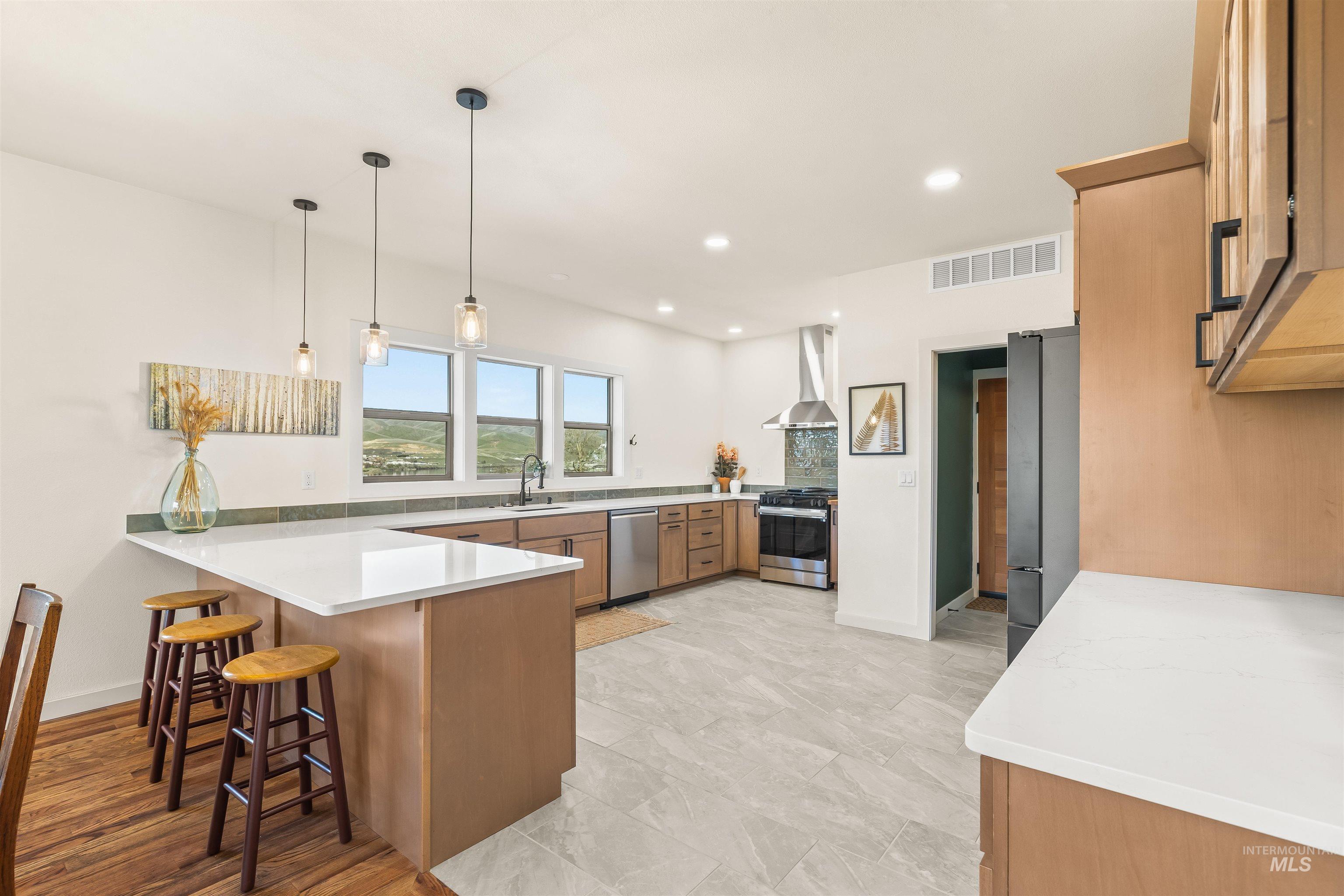 Kitchen with a peninsula, a kitchen bar, stainless steel appliances, hanging light fixtures, and wood finish cabinets