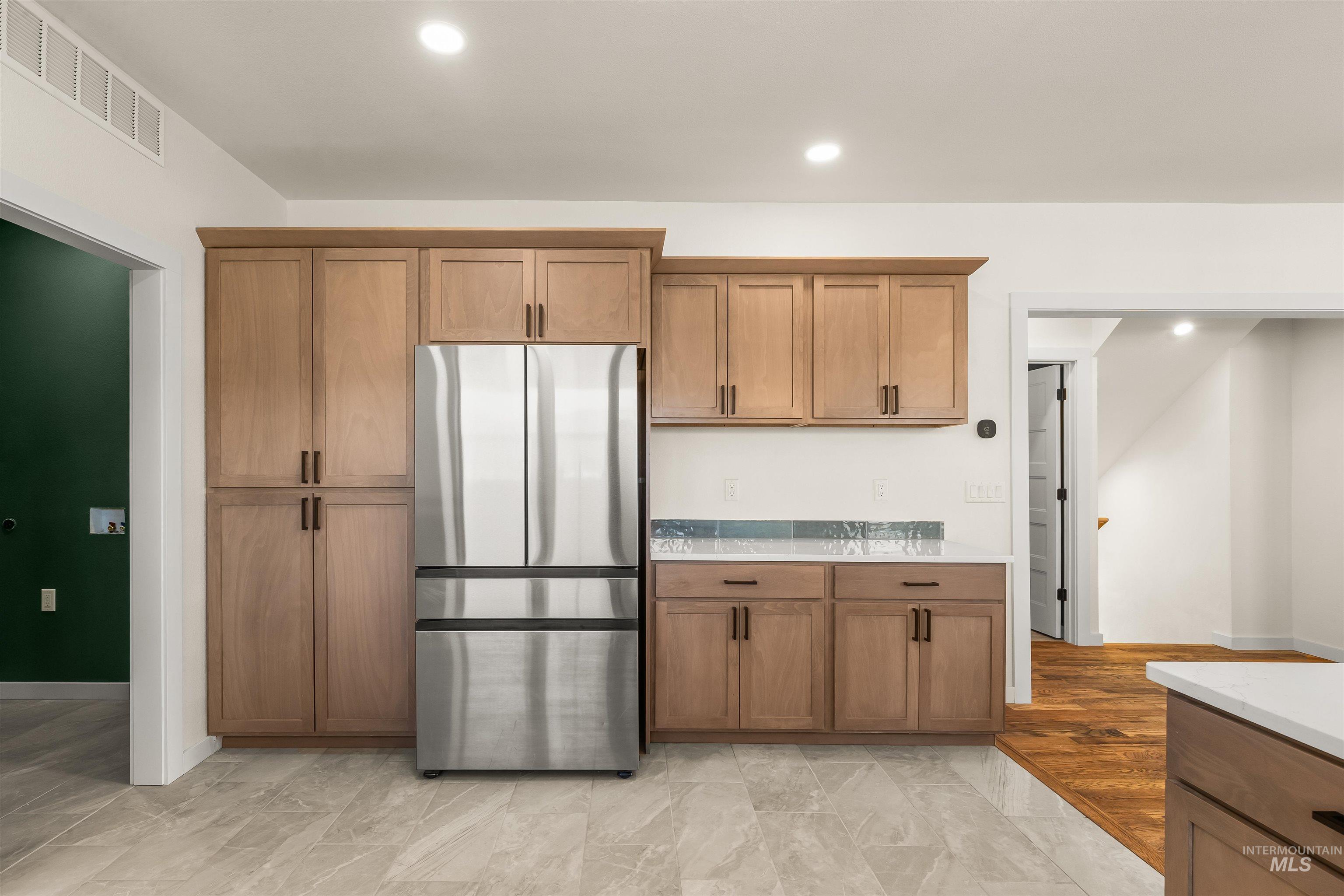 Kitchen with freestanding refrigerator, wood finish cabinetry, light stone countertops, and recessed lighting
