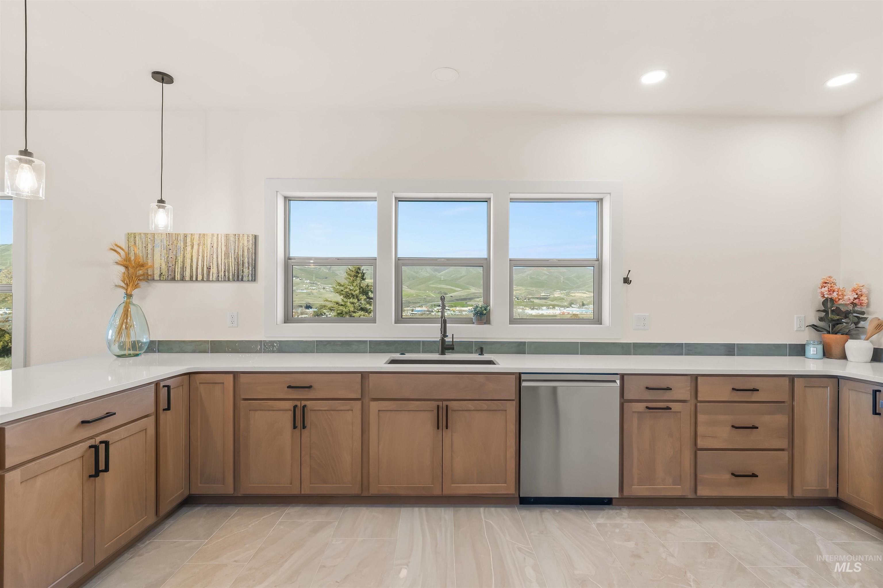 Kitchen with dishwasher, wood finish cabinets, hanging light fixtures, and light stone counters