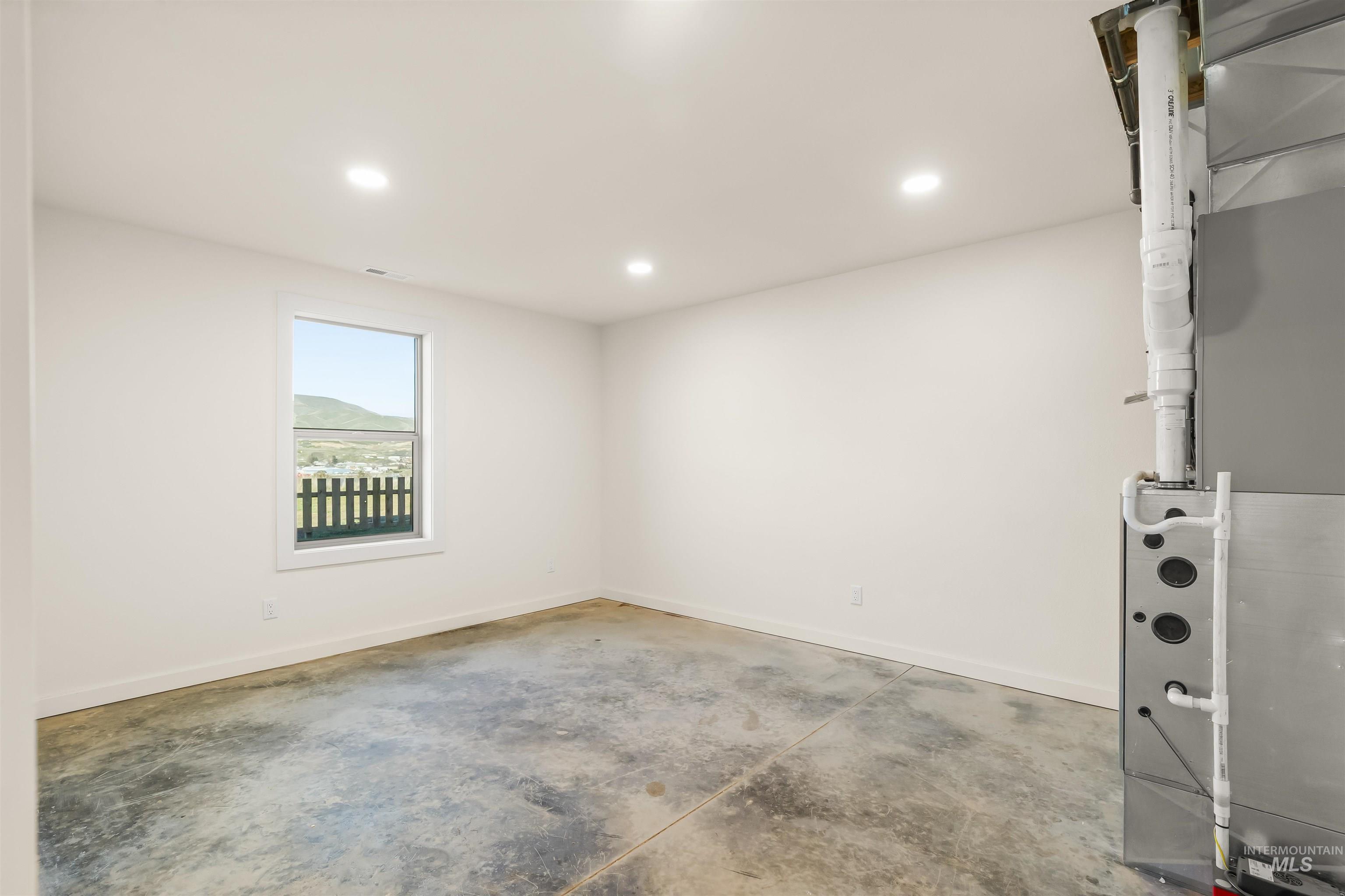 Unfurnished room featuring unfinished concrete floors, heating unit, and recessed lighting