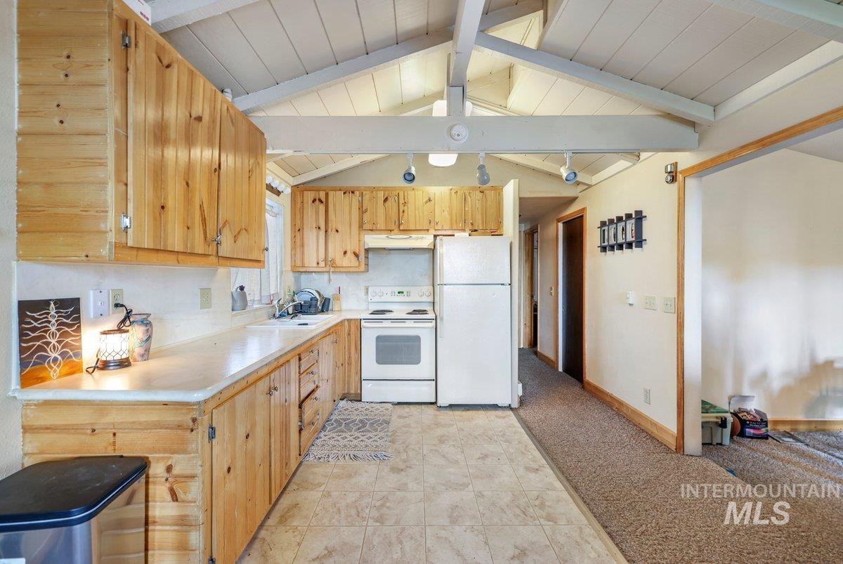 Kitchen with white appliances, light countertops, under cabinet range hood, and light brown cabinetry