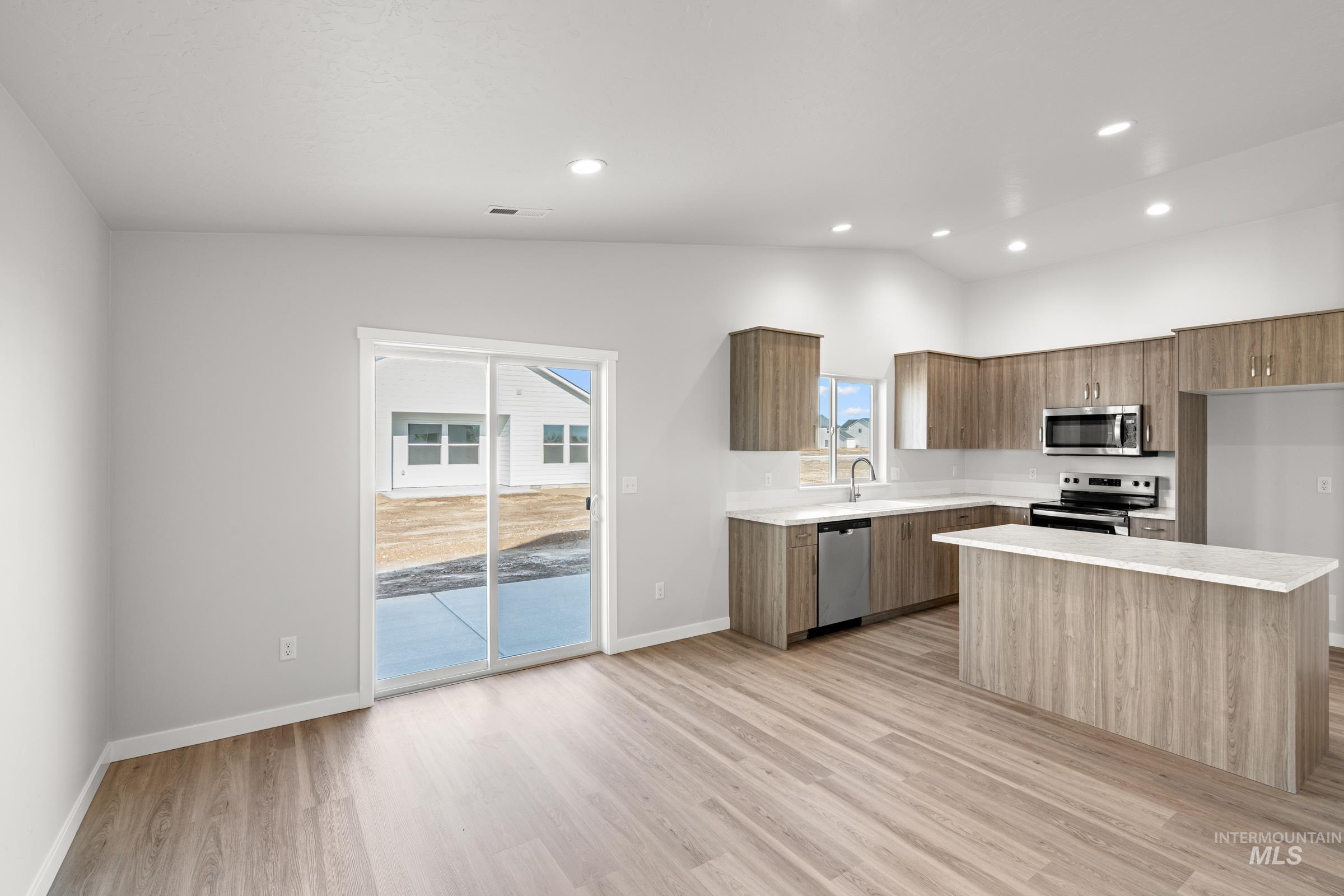 Kitchen with modern cabinets, stainless steel appliances, a center island, light wood-style floors, and vaulted ceiling