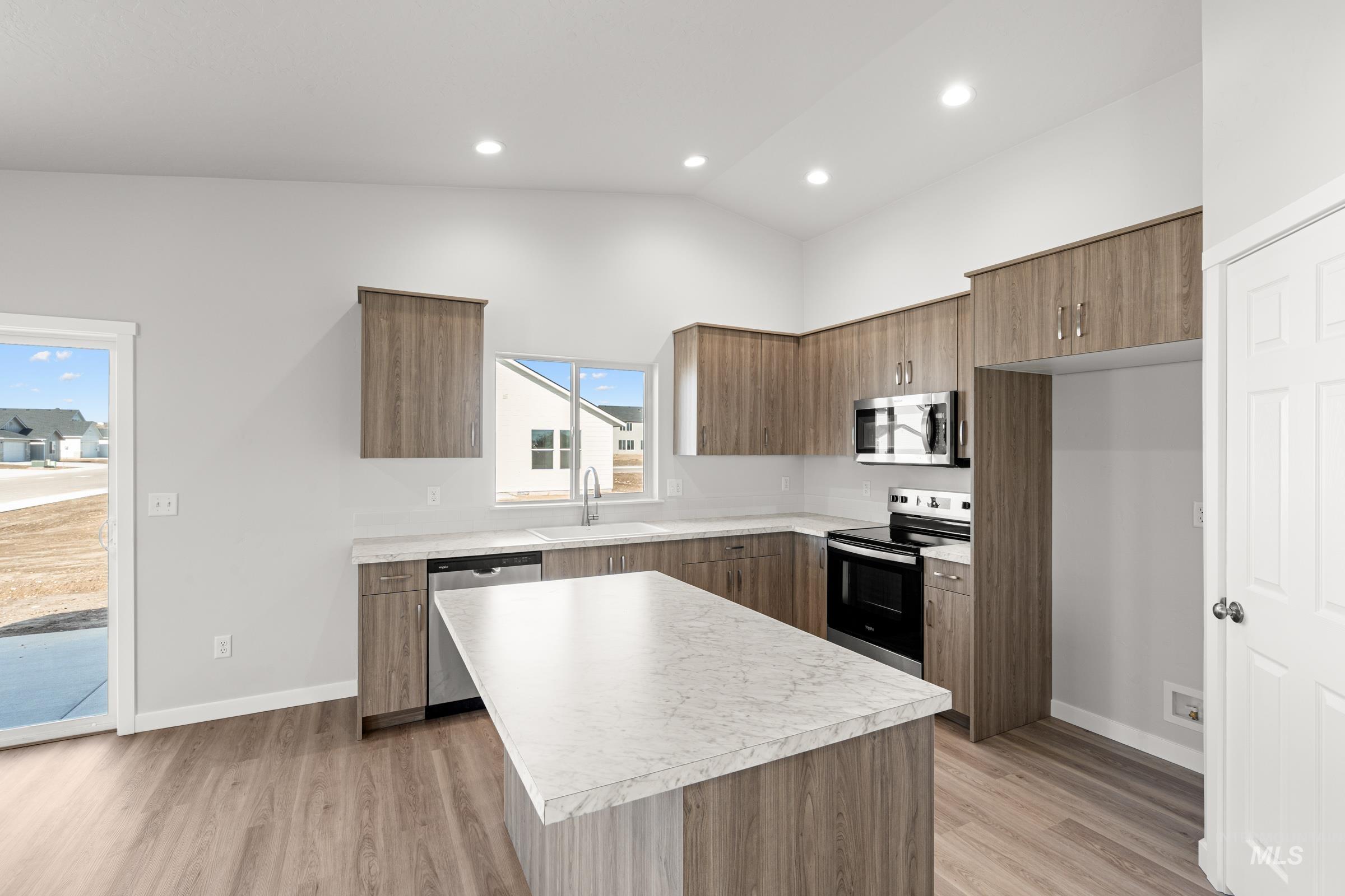 Kitchen featuring stainless steel appliances, a kitchen island, light countertops, light wood-style flooring, and lofted ceiling