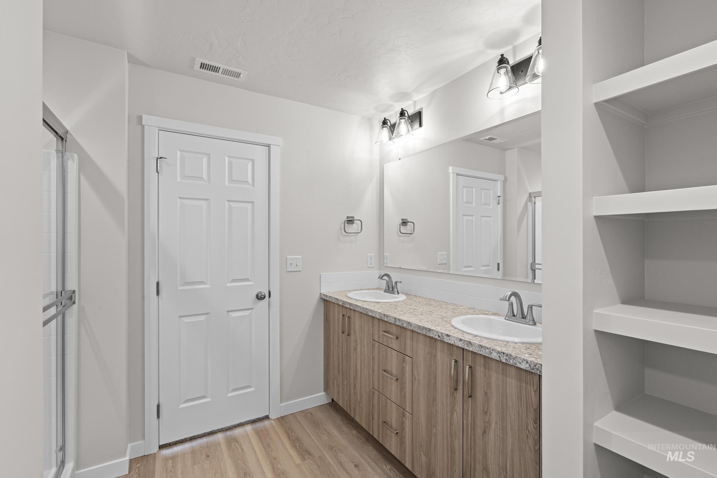 Bathroom with double vanity, light wood-type flooring, and a stall shower