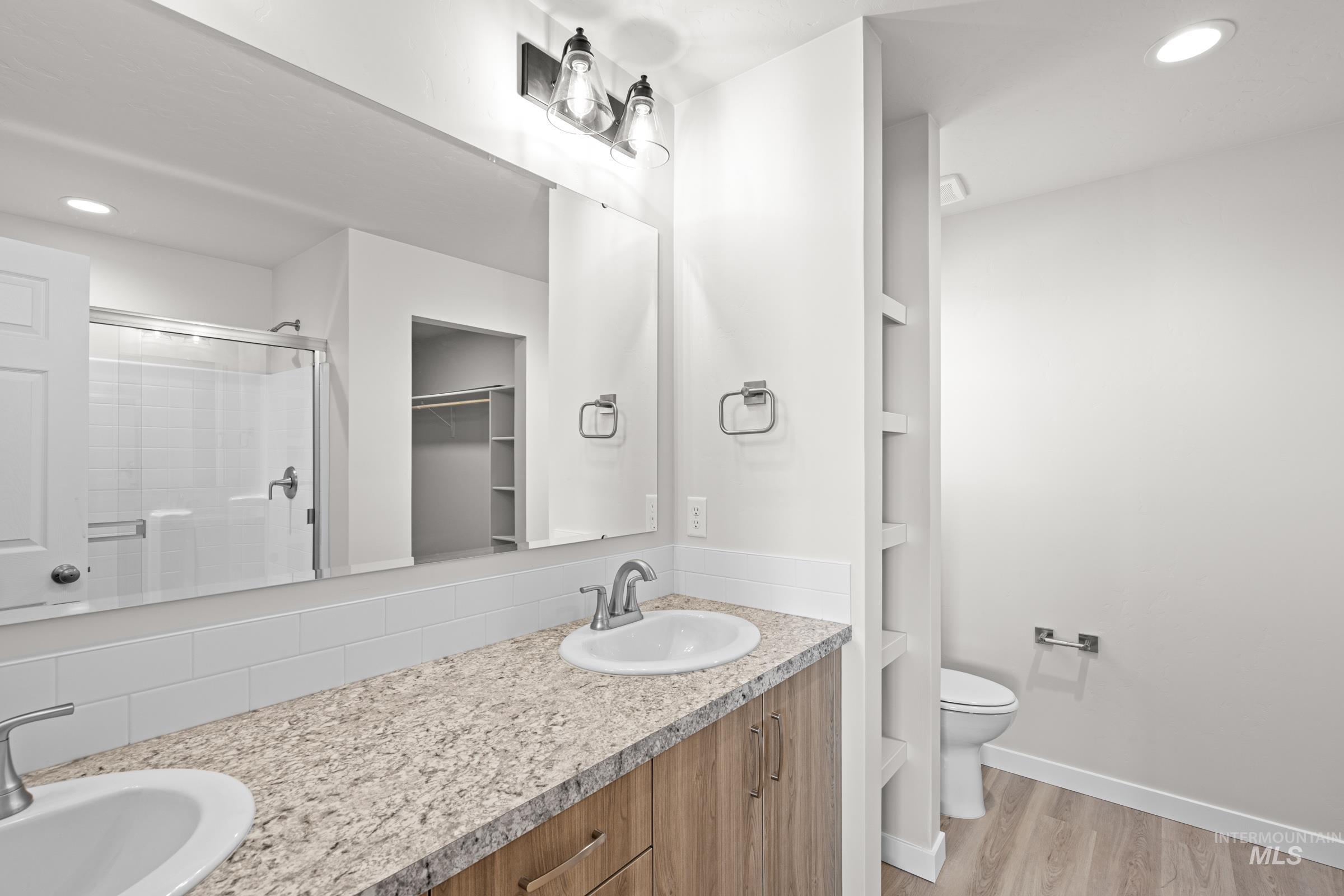 Bathroom with recessed lighting, double vanity, light wood finished floors, a shower stall, and a spacious closet