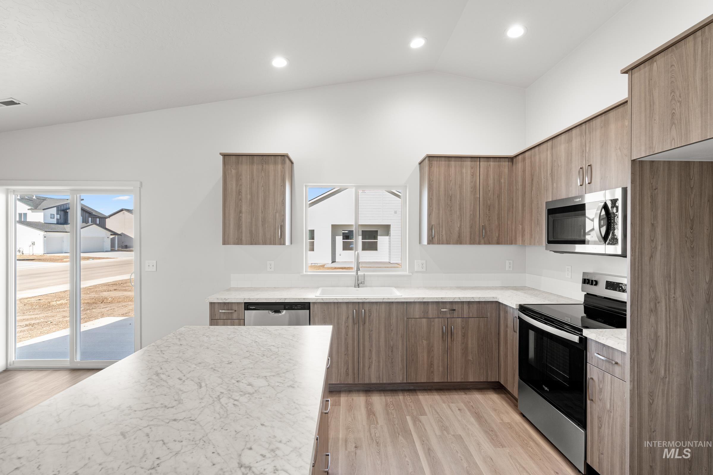 Kitchen with stainless steel appliances, vaulted ceiling, modern cabinets, light wood finished floors, and recessed lighting