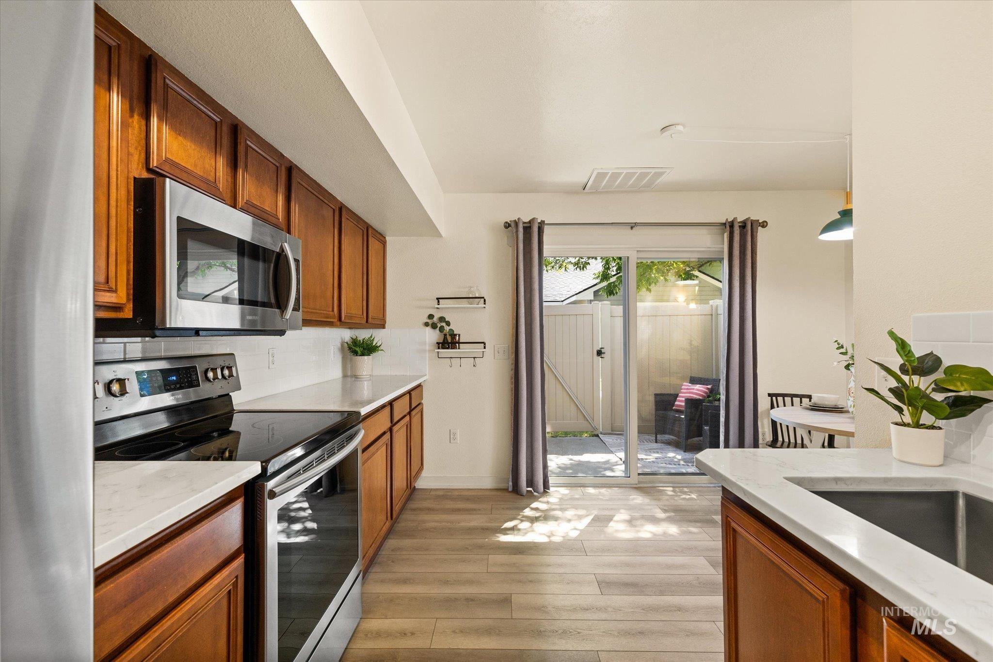 Kitchen with appliances with stainless steel finishes, light wood-type flooring, tasteful backsplash, light stone countertops, and brown cabinets