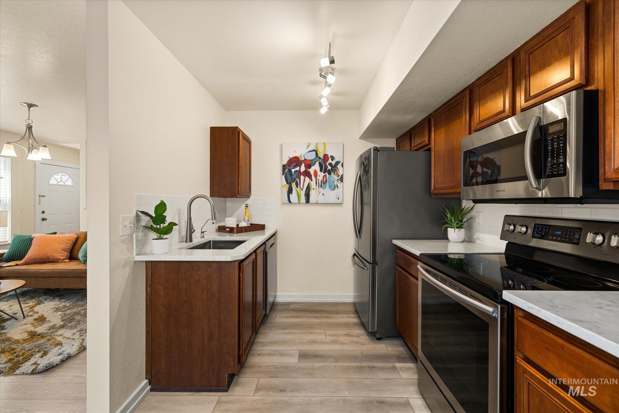 Kitchen with stainless steel appliances, light wood-style floors, light countertops, decorative backsplash, and rail lighting