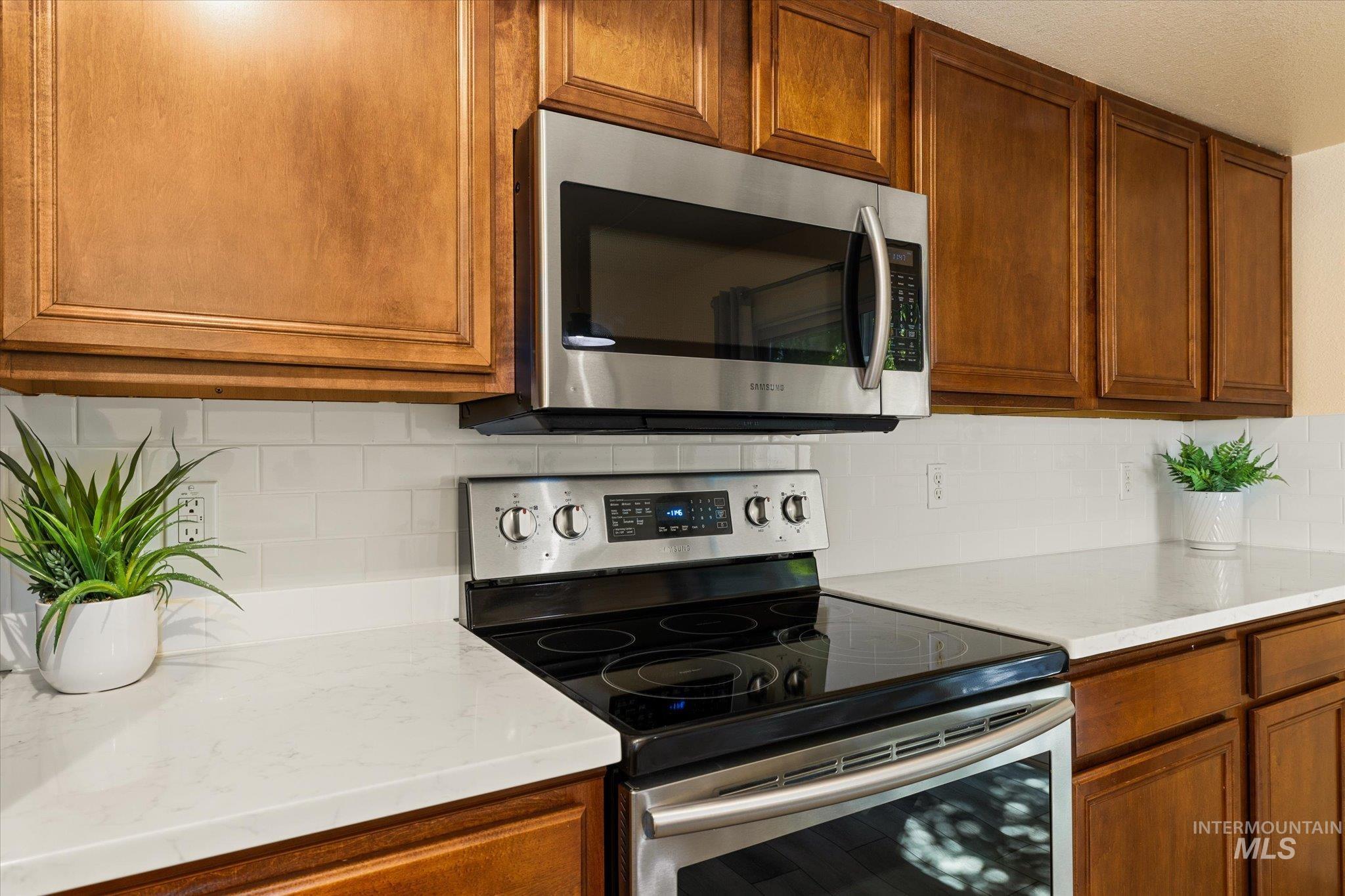 Kitchen with appliances with stainless steel finishes, light countertops, brown cabinetry, and tasteful backsplash