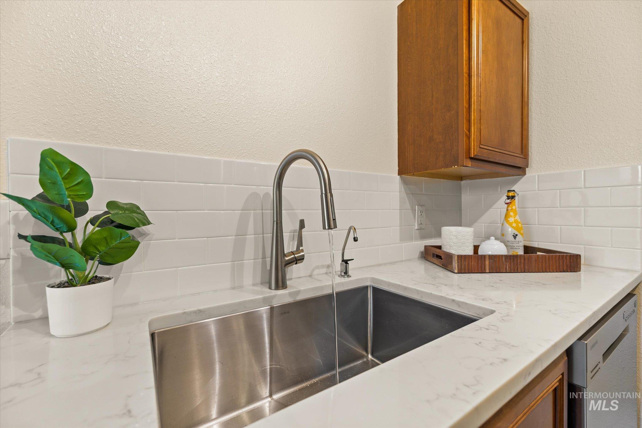 Kitchen with stainless steel dishwasher, brown cabinets, backsplash, and a textured wall