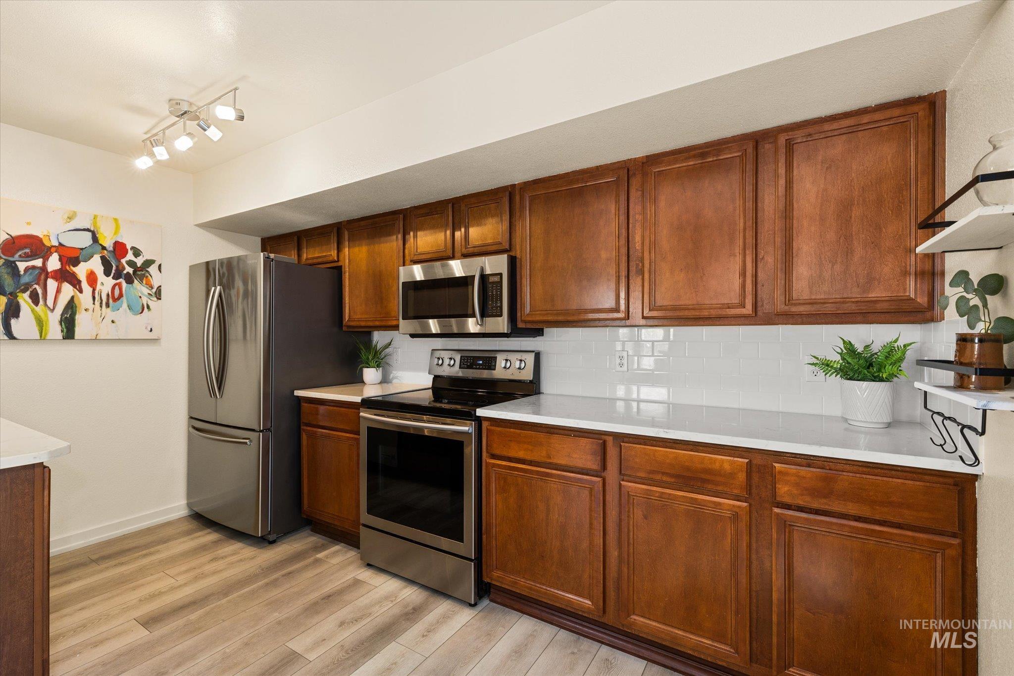 Kitchen featuring stainless steel appliances, light countertops, tasteful backsplash, and light wood finished floors