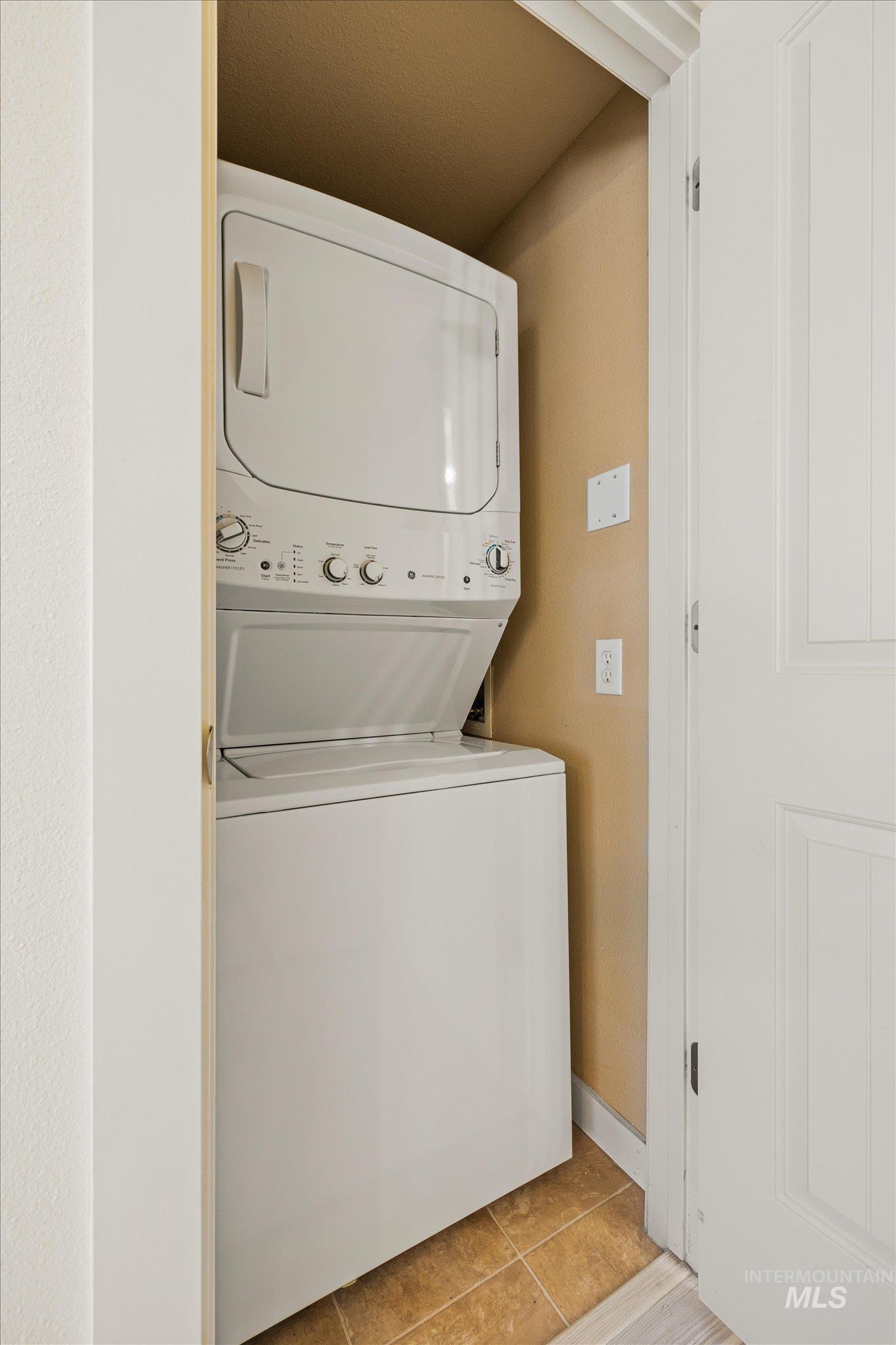 Laundry room with stacked washer / drying machine and light tile patterned floors