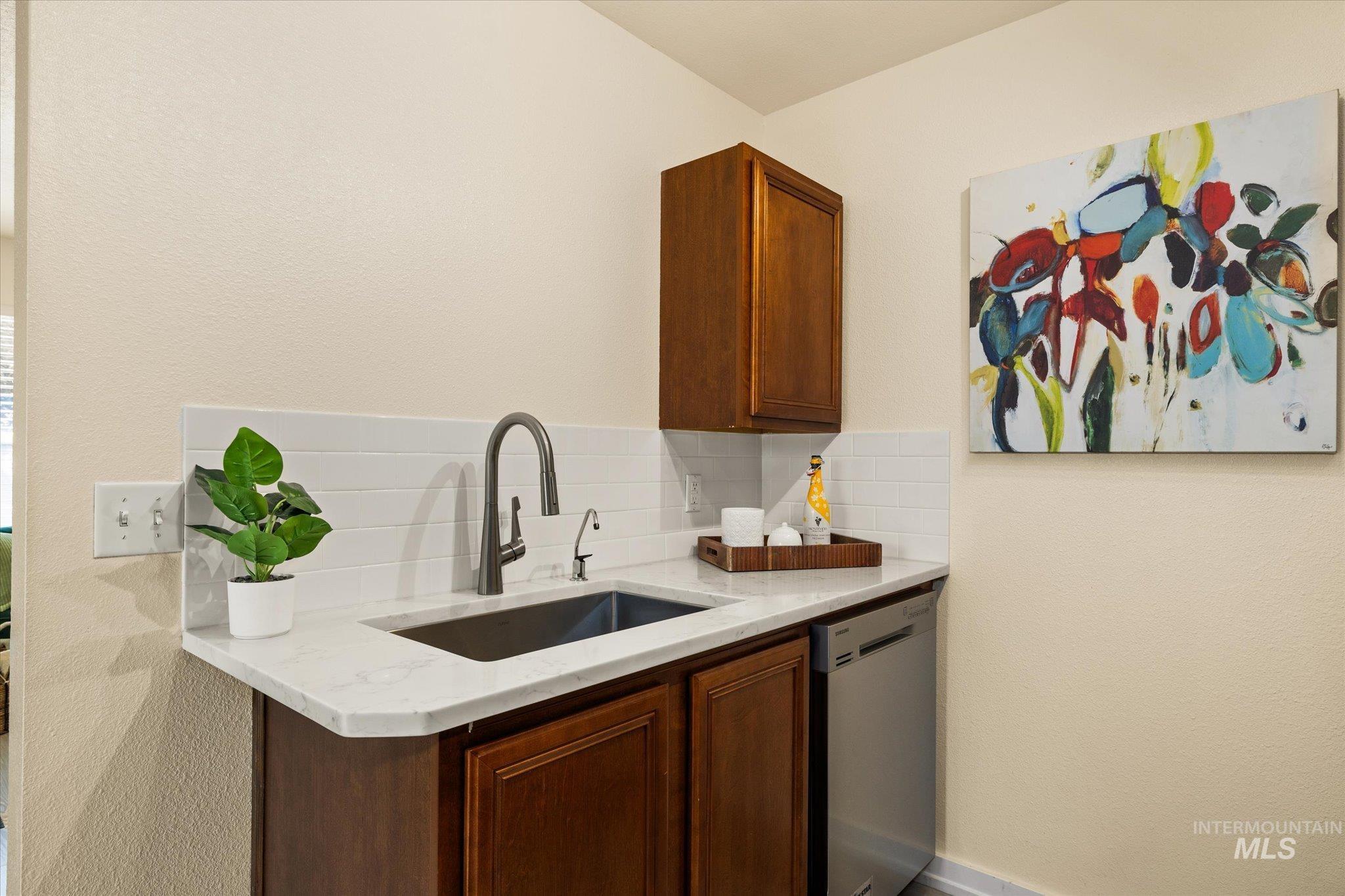 Kitchen with stainless steel dishwasher, decorative backsplash, and light stone countertops