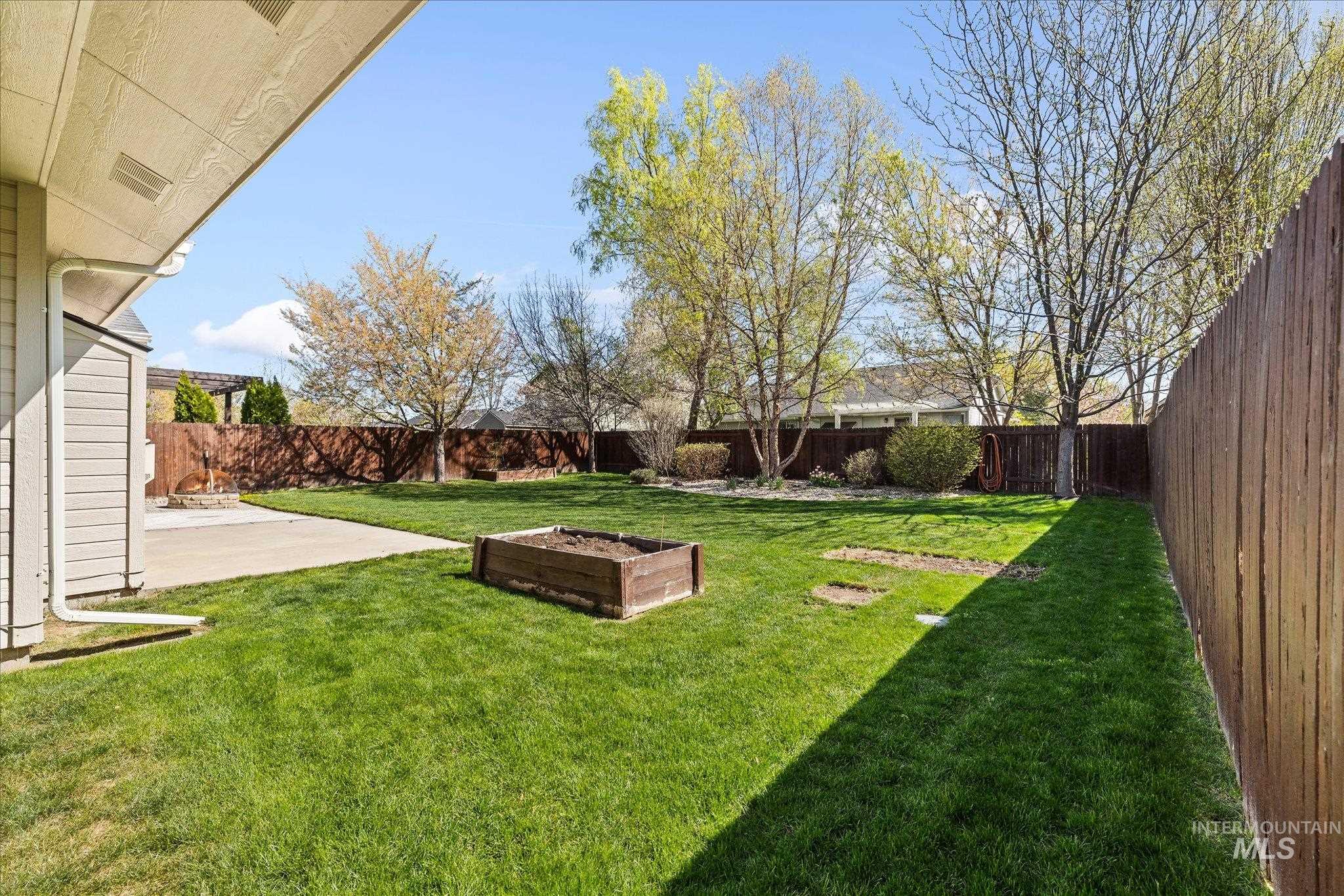 Fenced backyard with a patio area and a vegetable garden