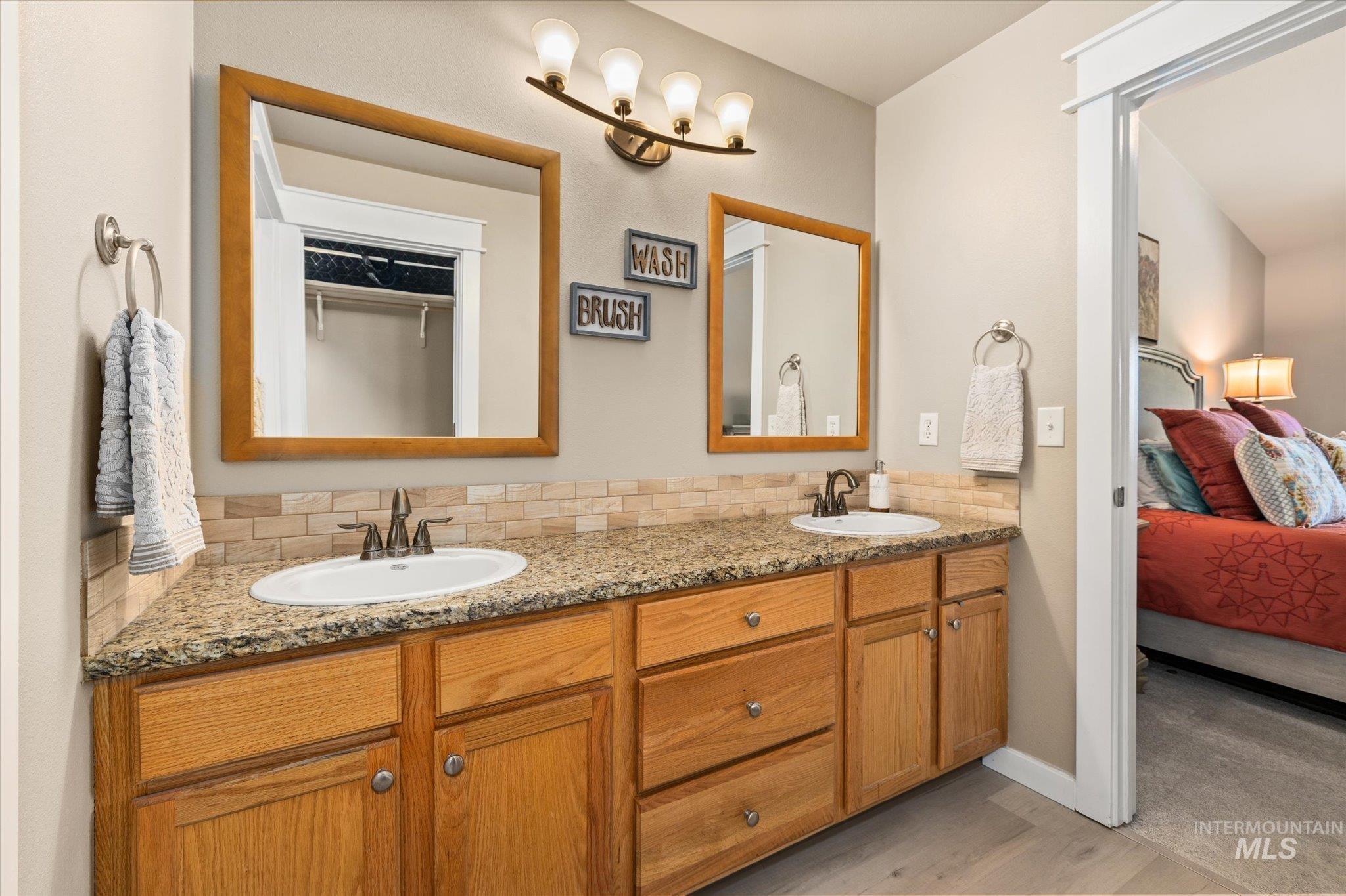 Ensuite bathroom with double vanity, decorative backsplash, and light wood-style floors