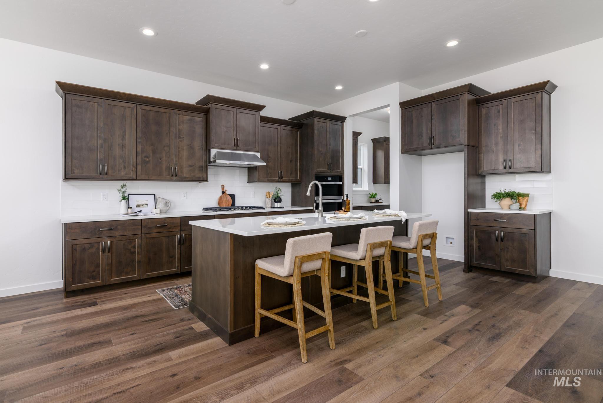 Kitchen featuring backsplash, a kitchen bar, recessed lighting, dark wood-type flooring, and a kitchen island with sink