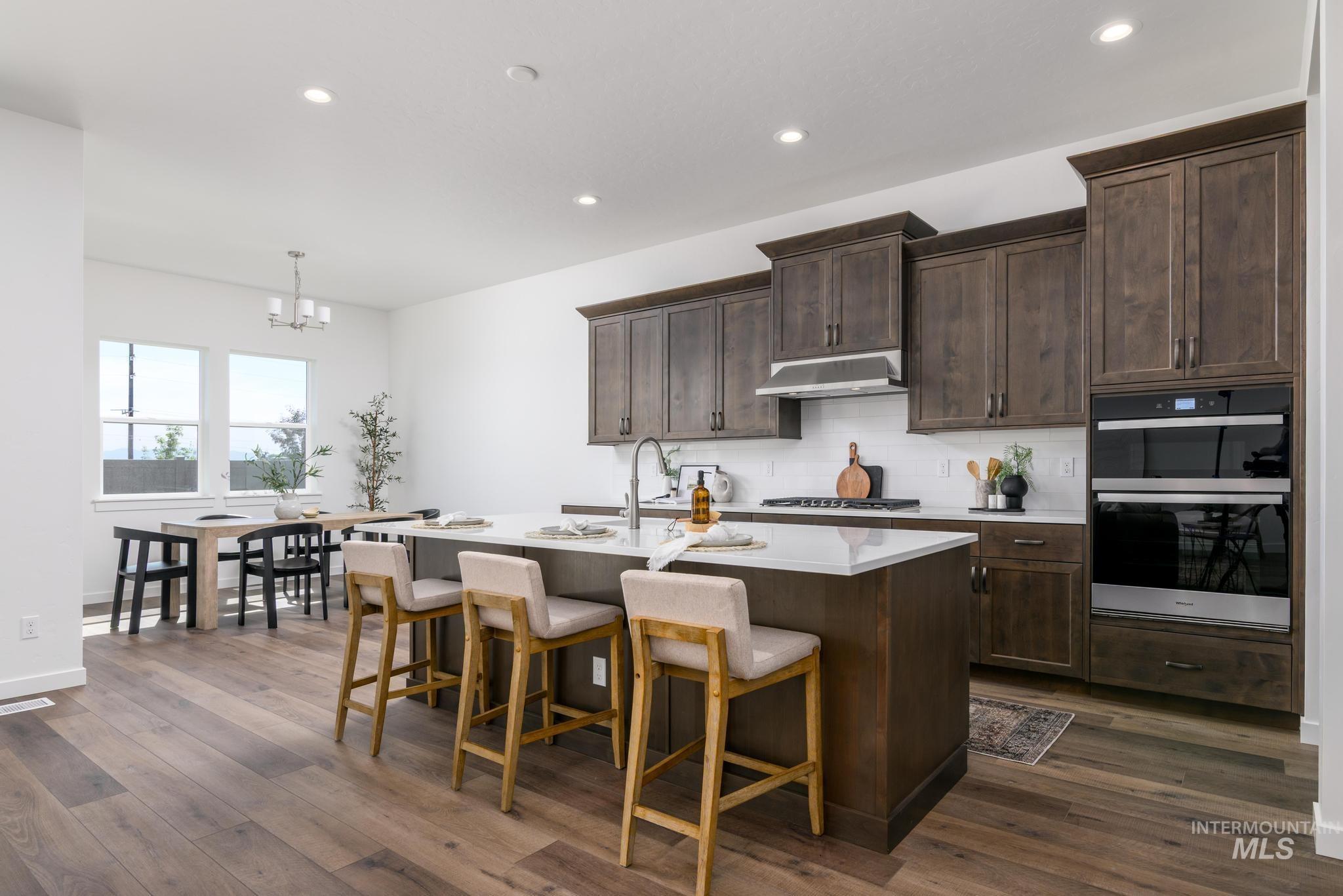 Kitchen featuring backsplash, hanging light fixtures, recessed lighting, an island with sink, and a breakfast bar area