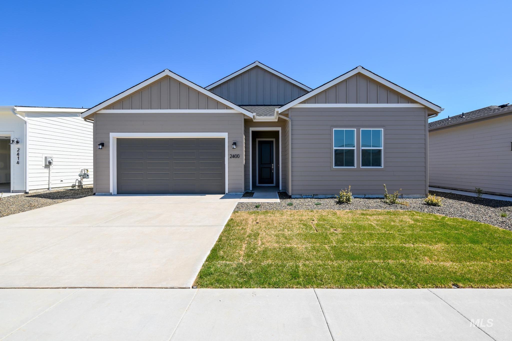 View of front of home with board and batten siding, driveway, an attached garage, and a front lawn