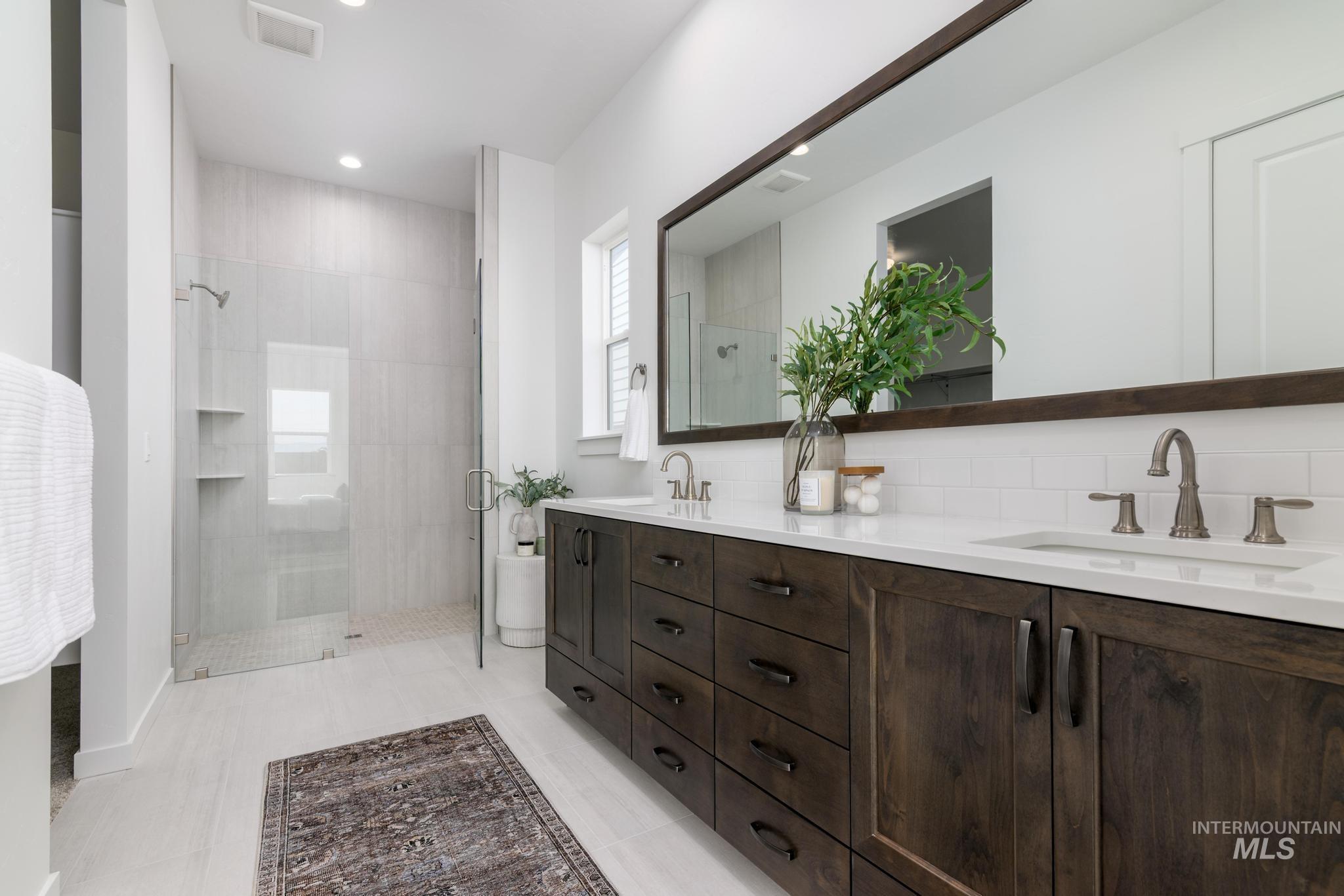 Bathroom featuring a stall shower, double vanity, decorative backsplash, light tile patterned flooring, and recessed lighting