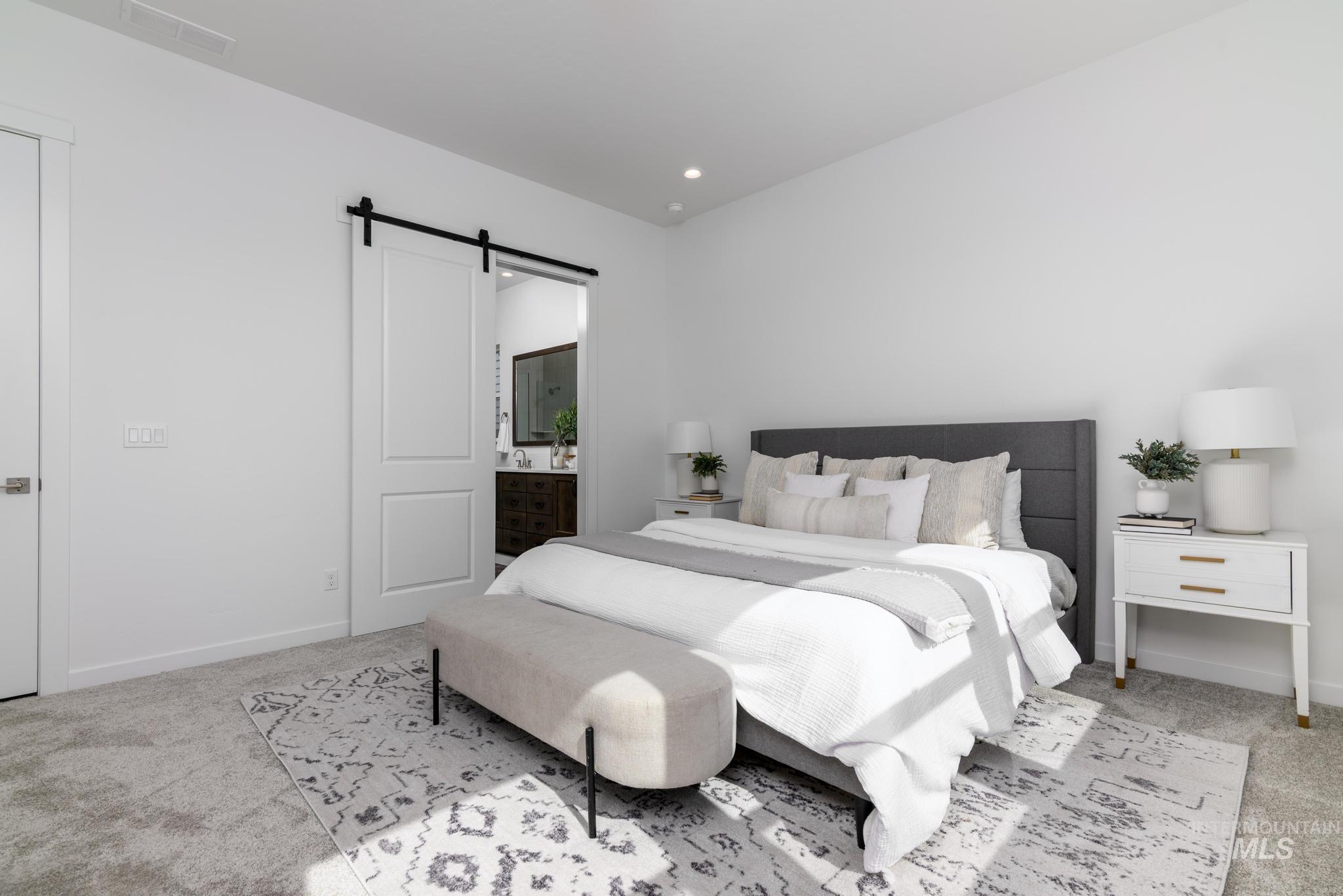 Bedroom with light colored carpet, a barn door, connected bathroom, and recessed lighting