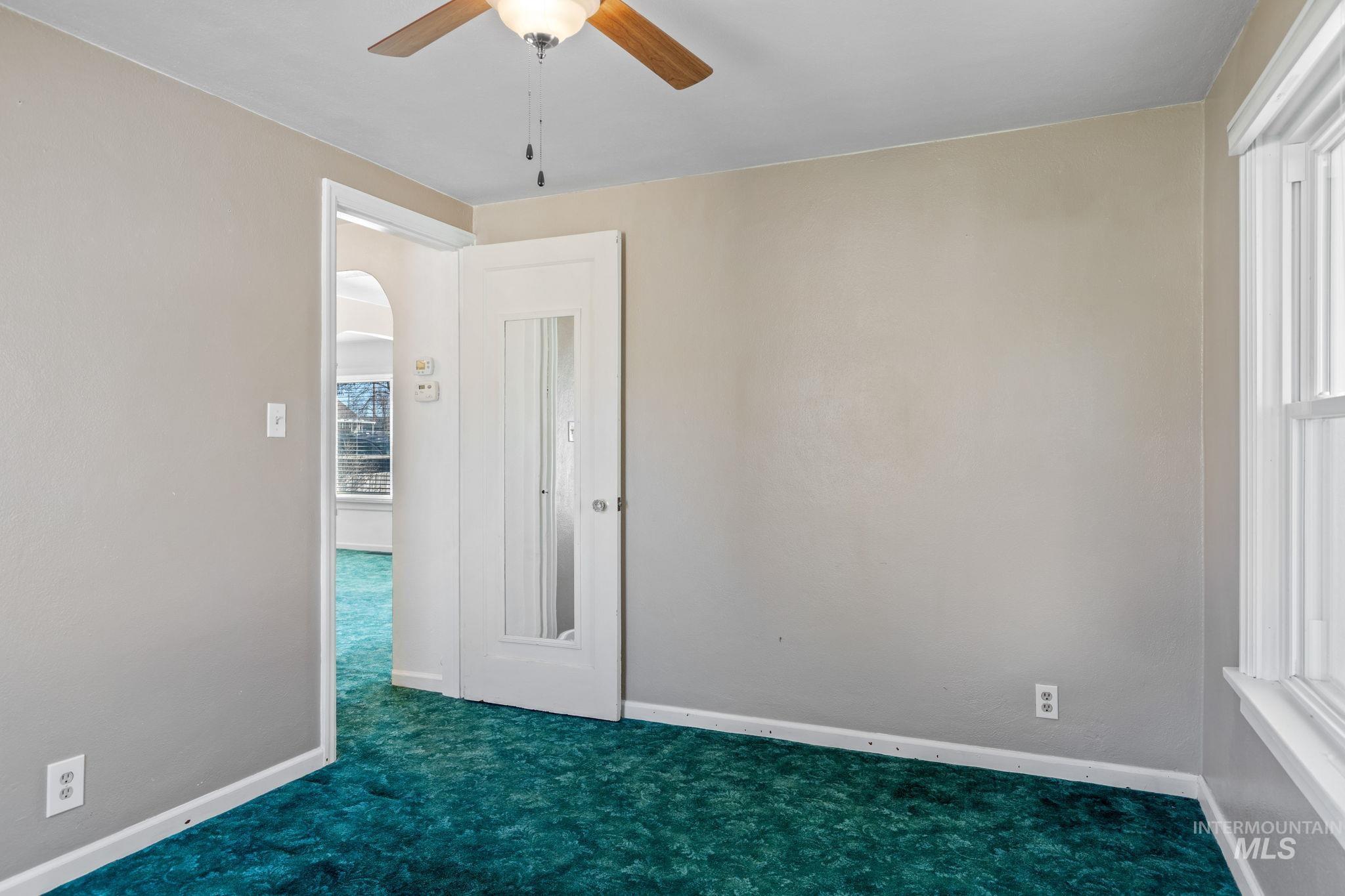 Empty room featuring a ceiling fan, arched walkways, and carpet flooring