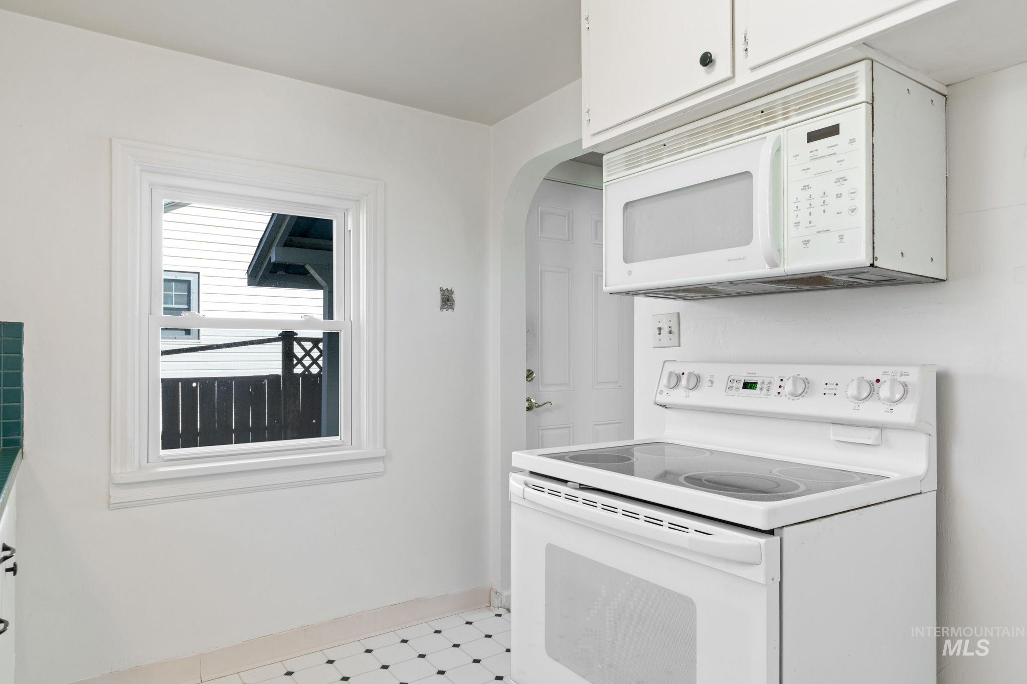 Kitchen with white appliances, white cabinetry, light countertops, arched walkways, and light flooring