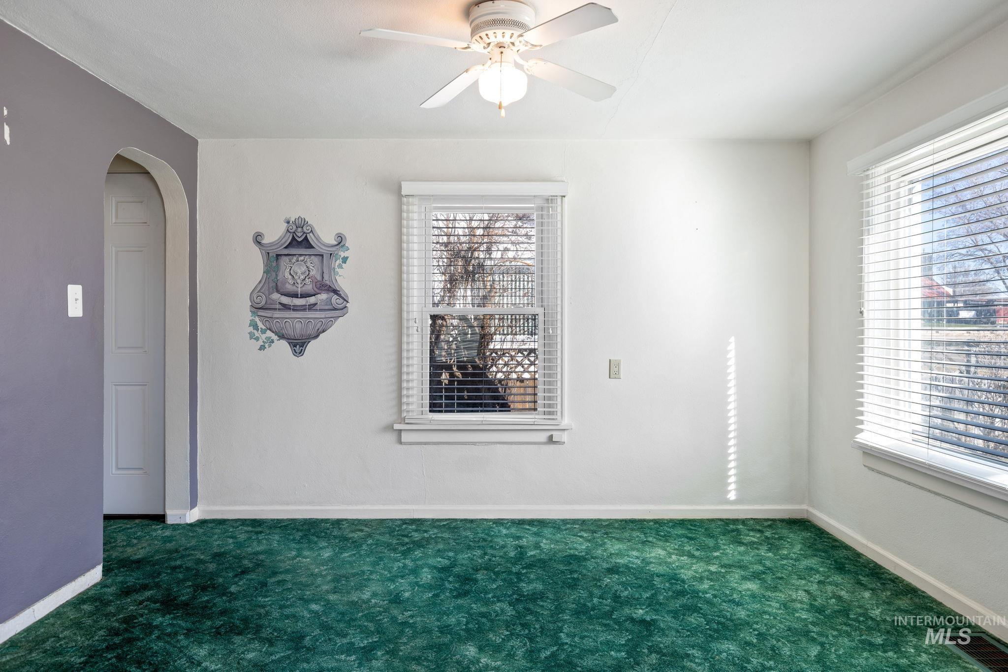 Carpeted empty room featuring arched walkways and a ceiling fan