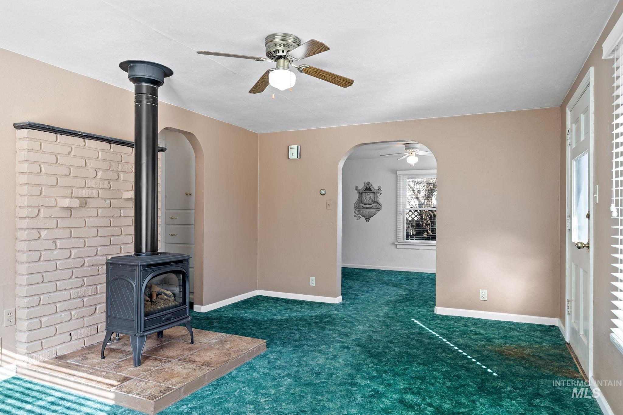Unfurnished living room with ceiling fan, arched walkways, carpet, and a wood stove