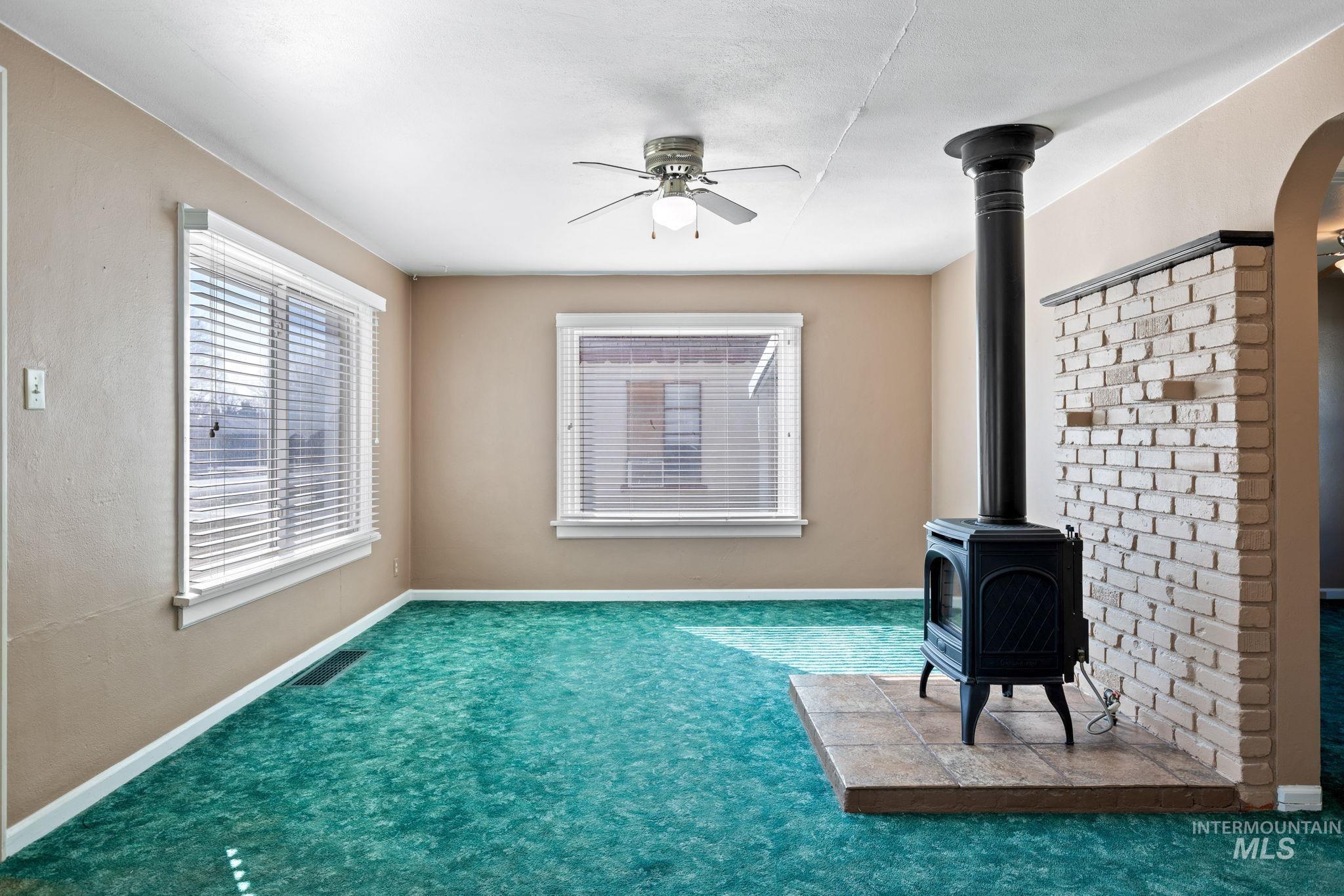 Unfurnished living room featuring ceiling fan, a wood stove, and carpet