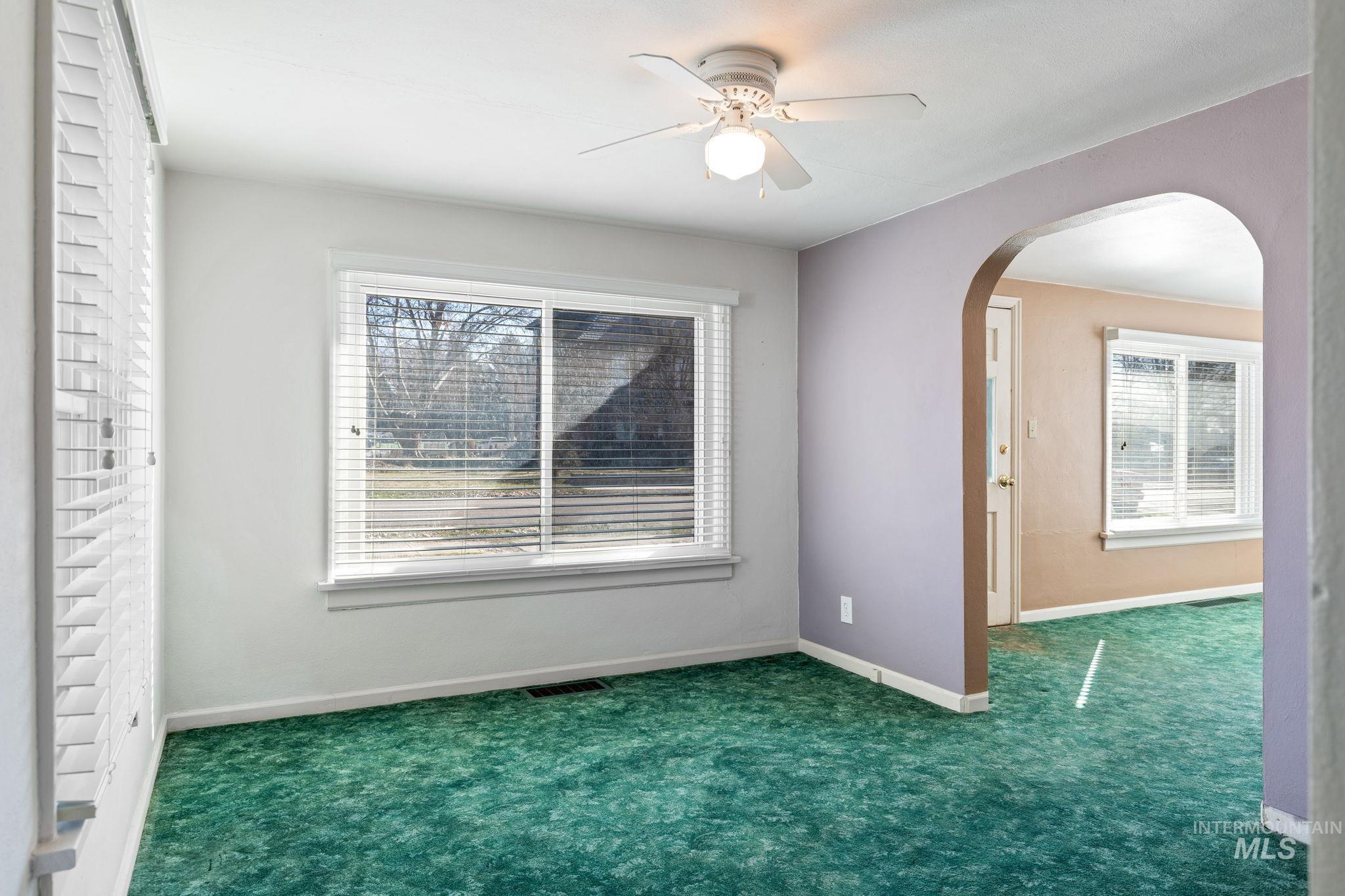 Empty room featuring ceiling fan, carpet flooring, and arched walkways