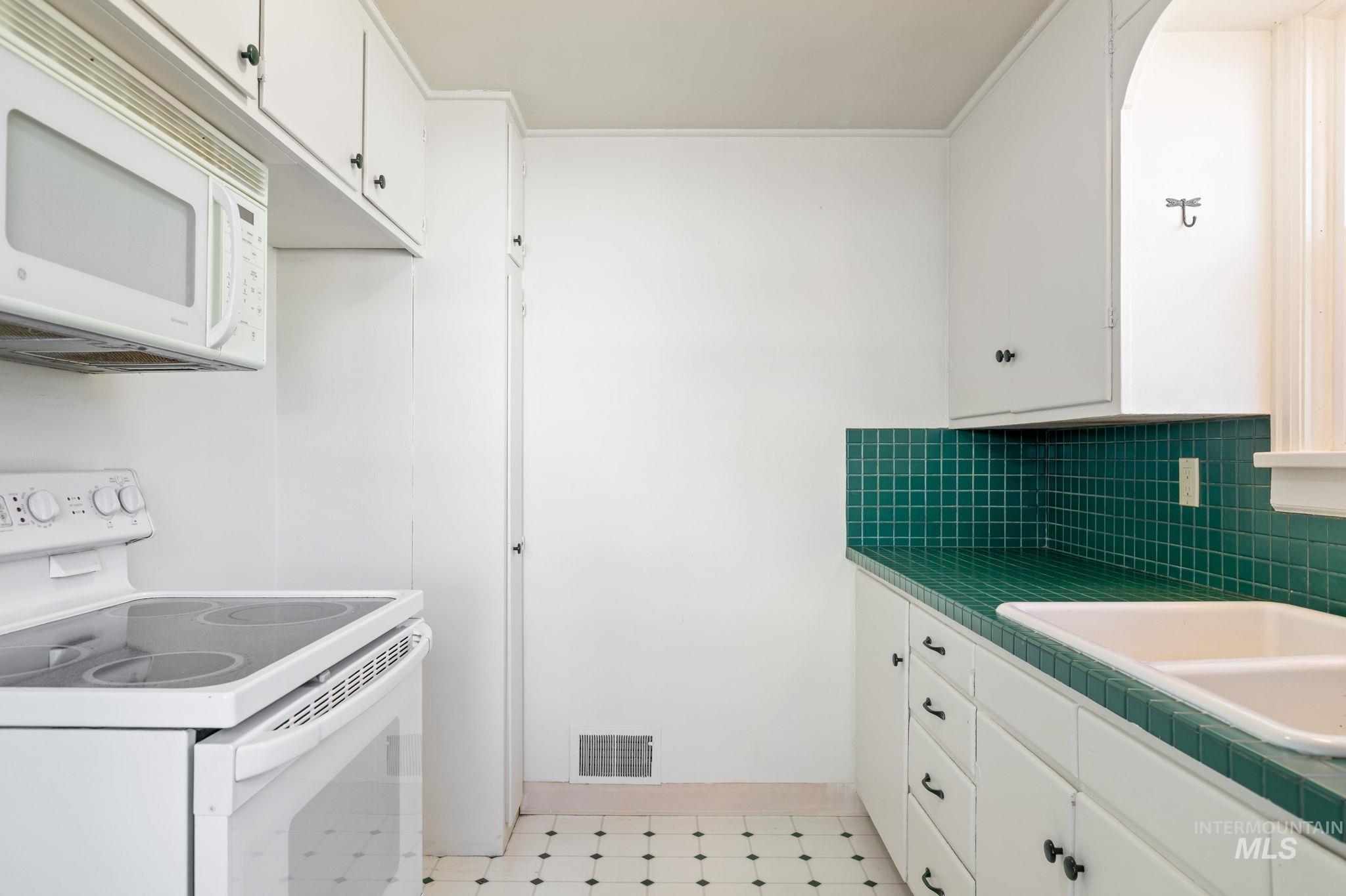 Kitchen with white appliances, tile counters, light flooring, and white cabinets