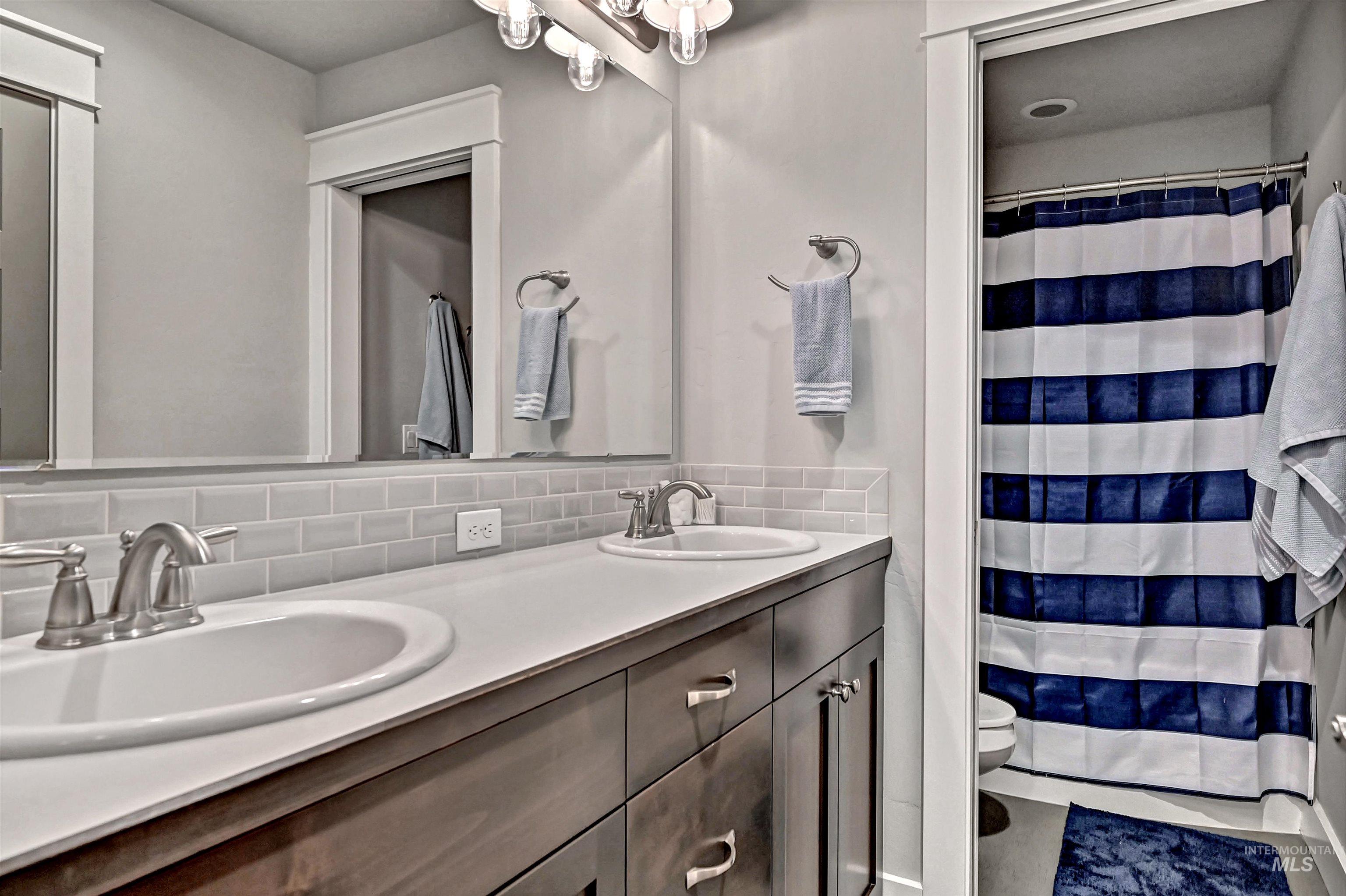 Bathroom with double vanity, a shower with shower curtain, and tasteful backsplash