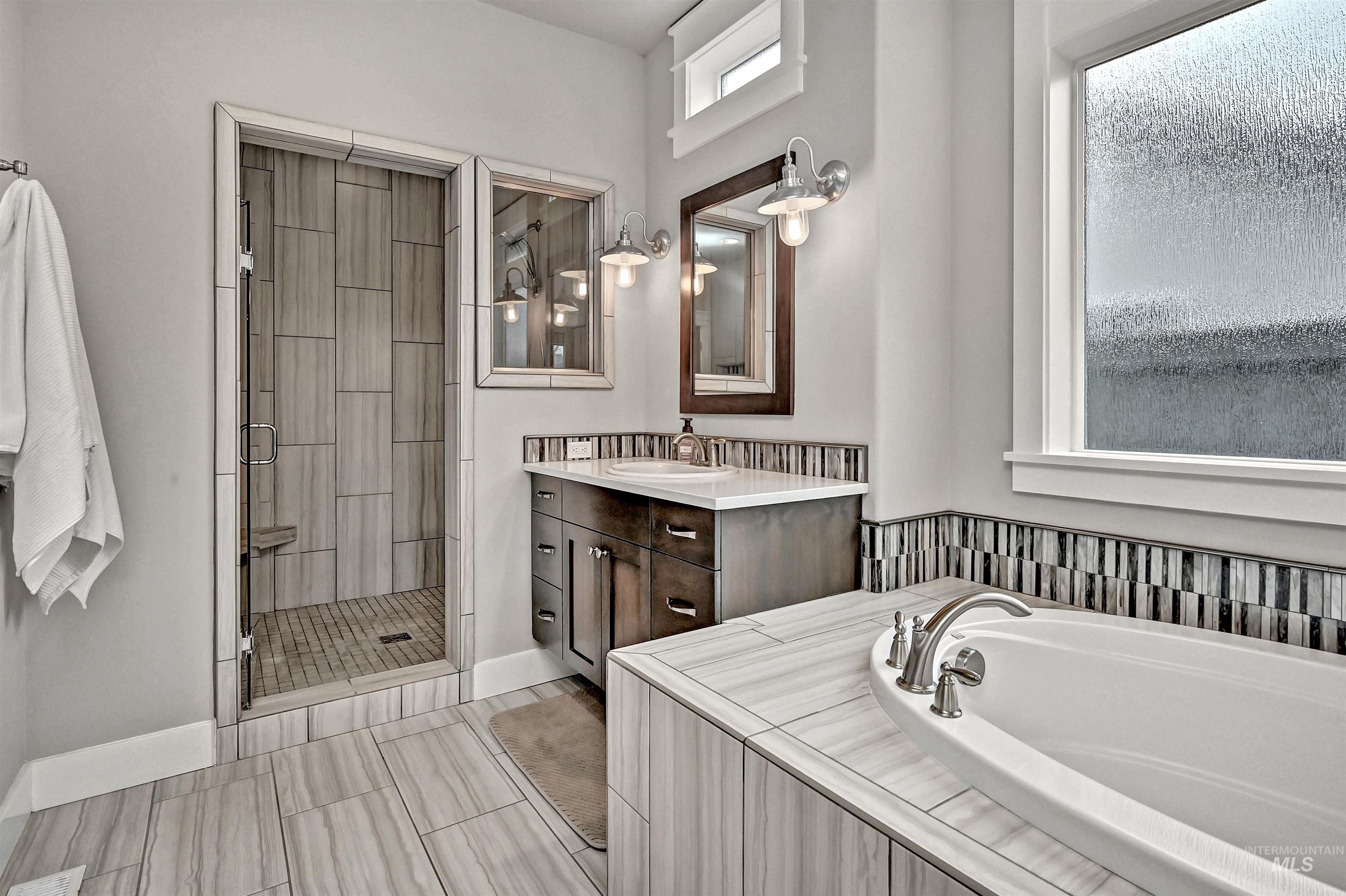 Ensuite bathroom featuring two floating vanities, a large soaker tub, walk-in tile shower, and plenty of natural light