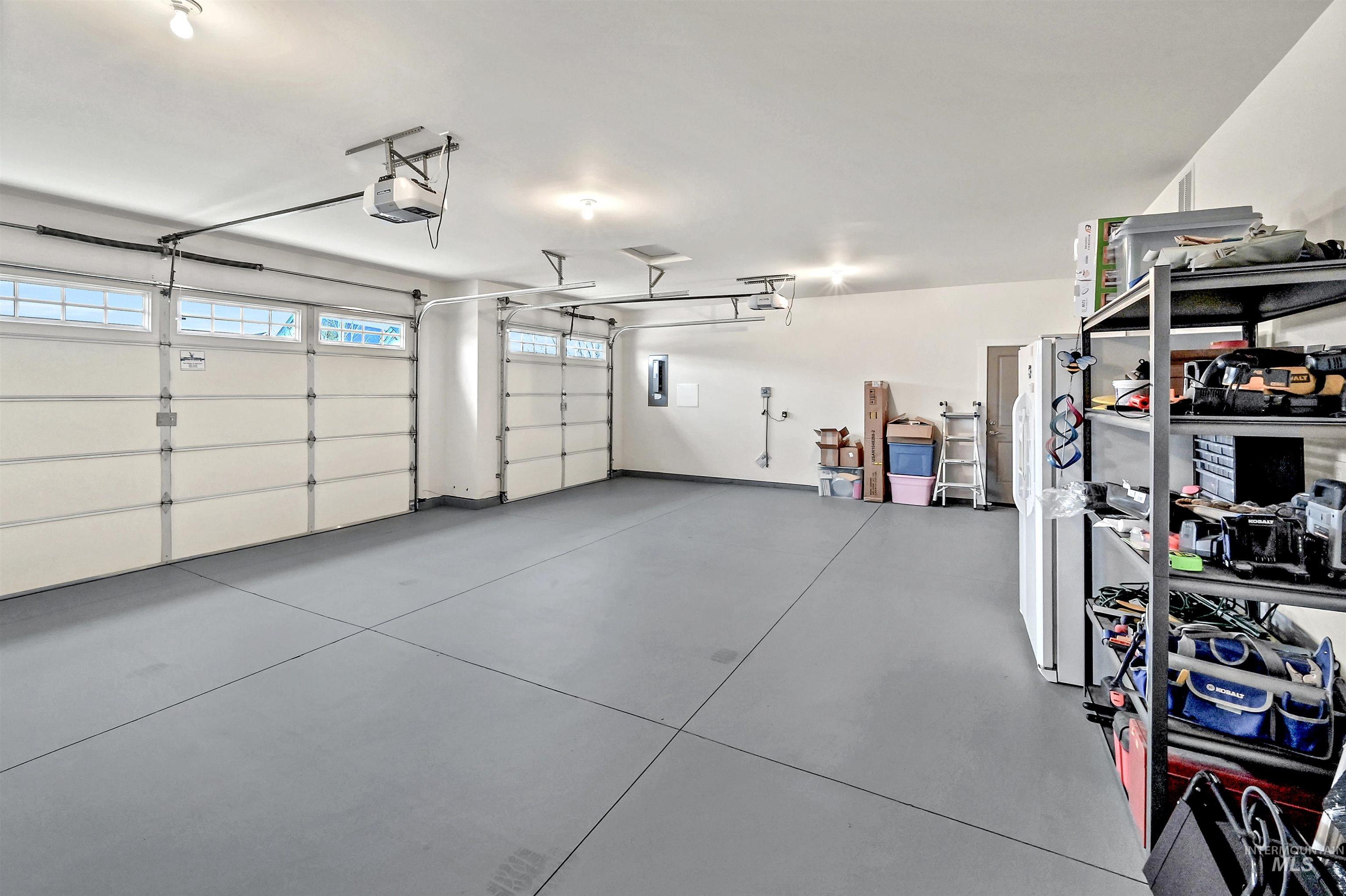 3-car attached garage featuring a garage door opener, electric panel, and painted floor