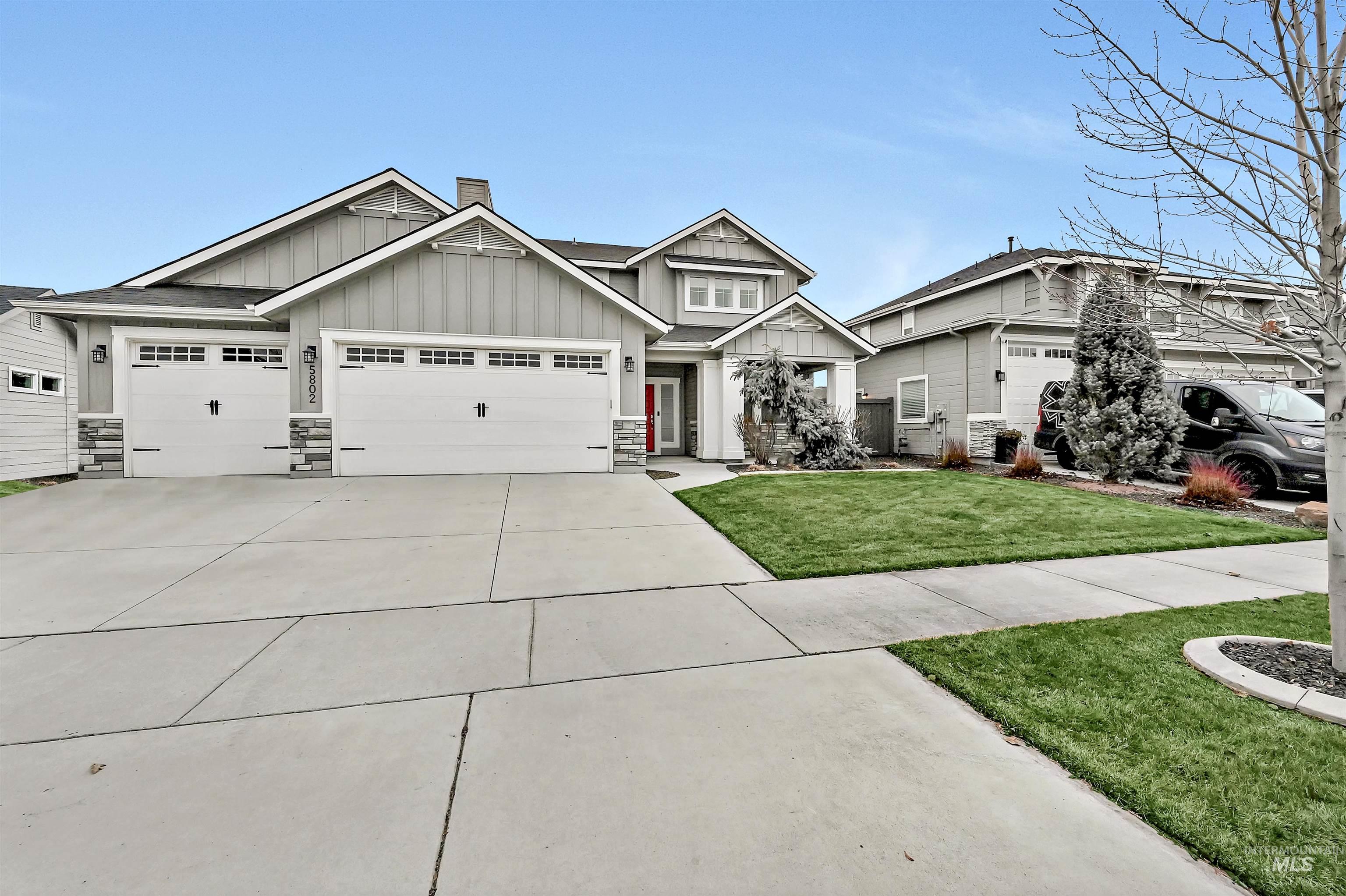 Craftsman inspired home featuring board and batten siding, a large concrete driveway, a front lawn, a 3-car garage, and stone accents