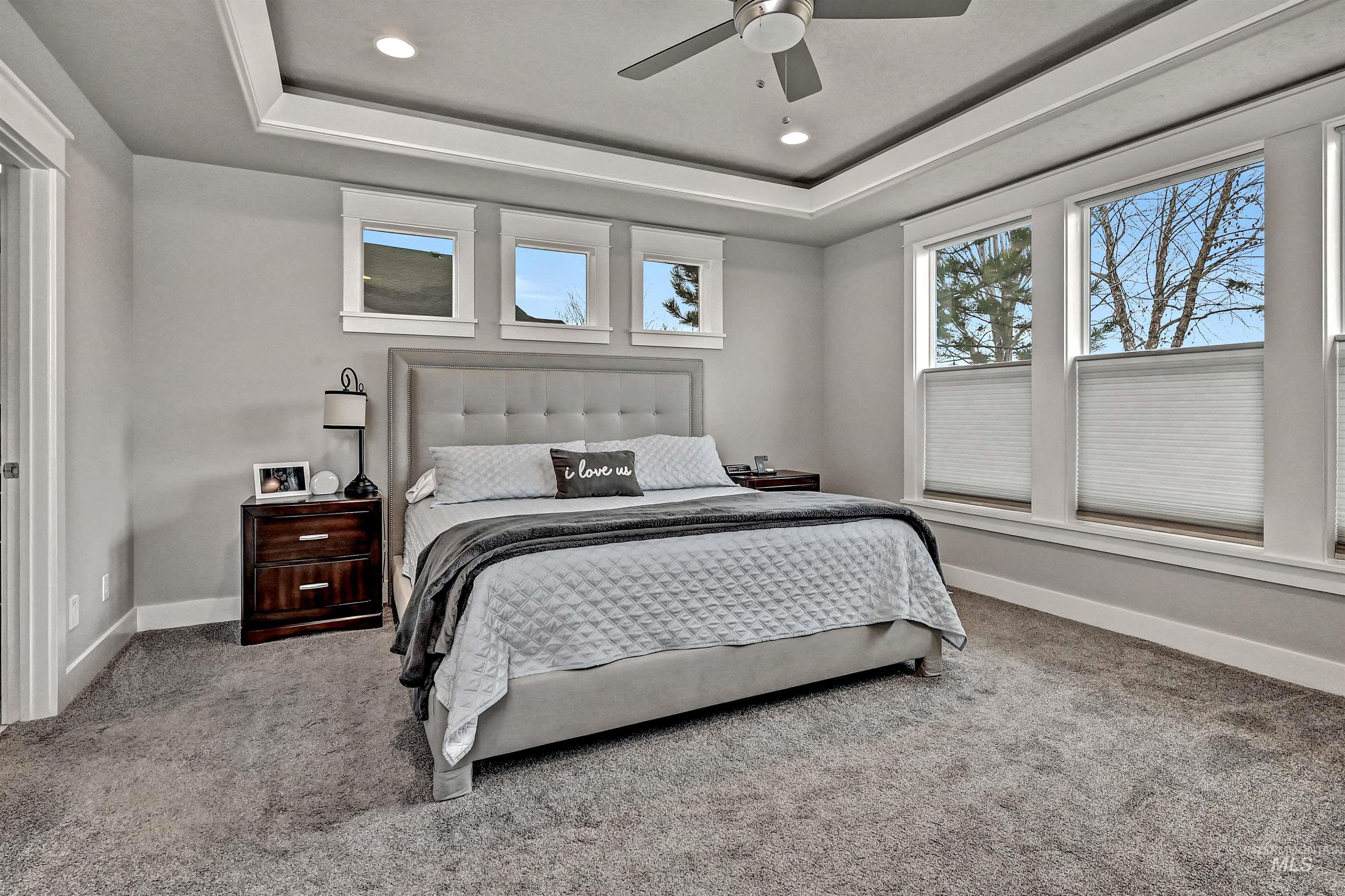 Primary bedroom with light colored carpet, recessed lighting, a ceiling fan, and a tray ceiling