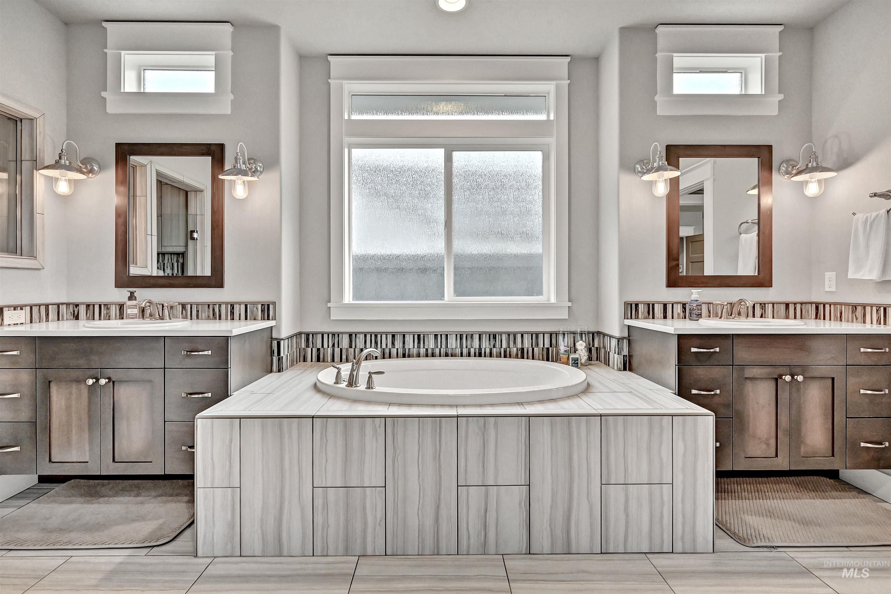 Ensuite bathroom featuring two floating vanities, a large soaker tub, and plenty of natural light