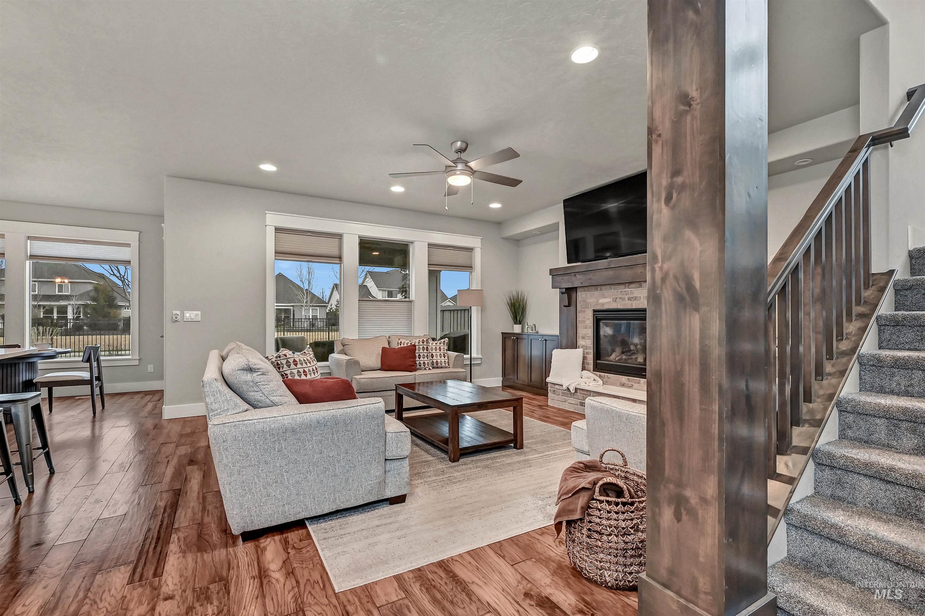 View into the great room and fireplace from the base of the stairwell leading upstairs, large windows, wood banister, and out to the backyard.