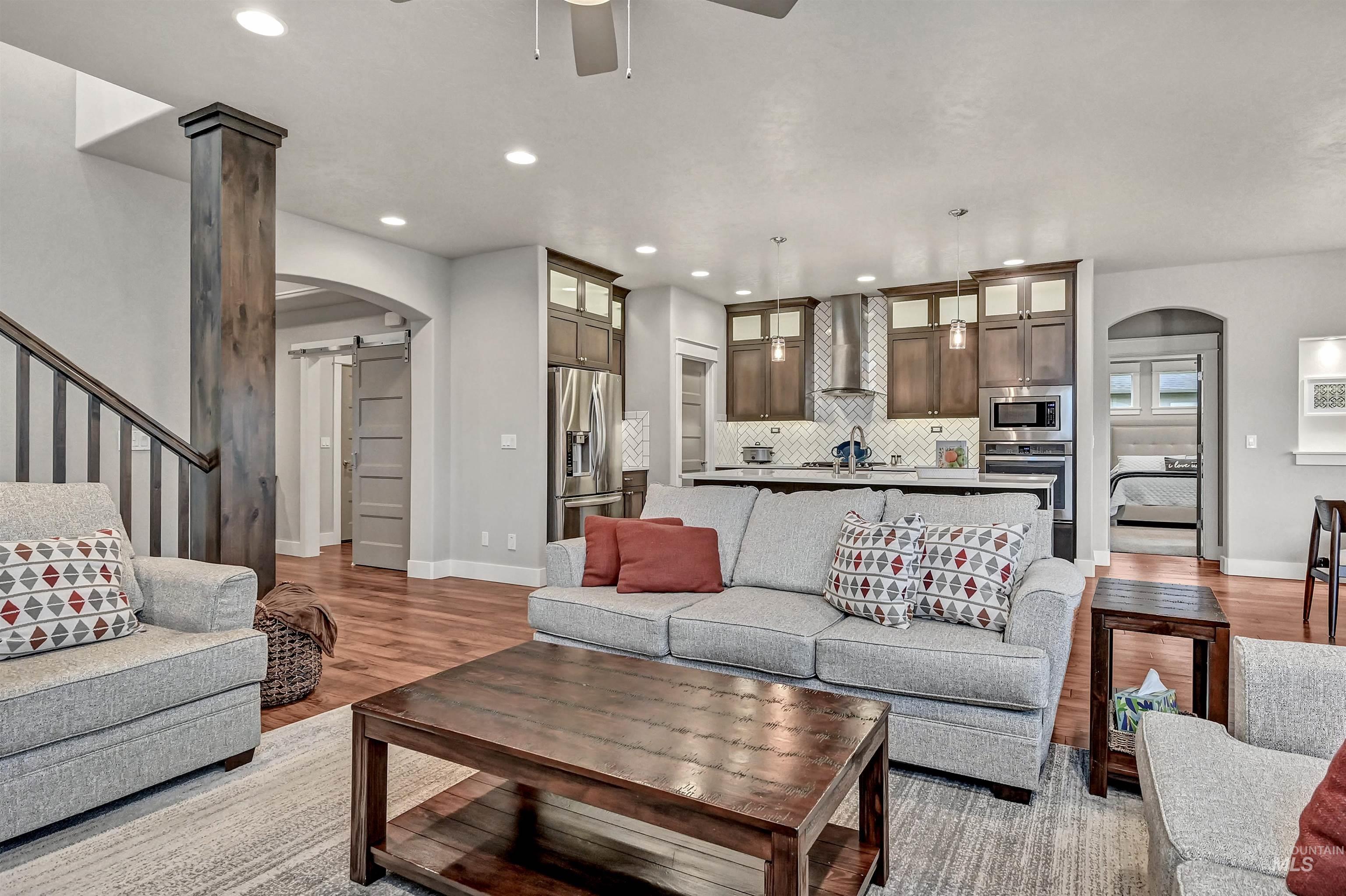 Open-style great room featuring engineered-wood flooring, a ceiling fan, a view into the kitchen & dining area, and recessed lighting