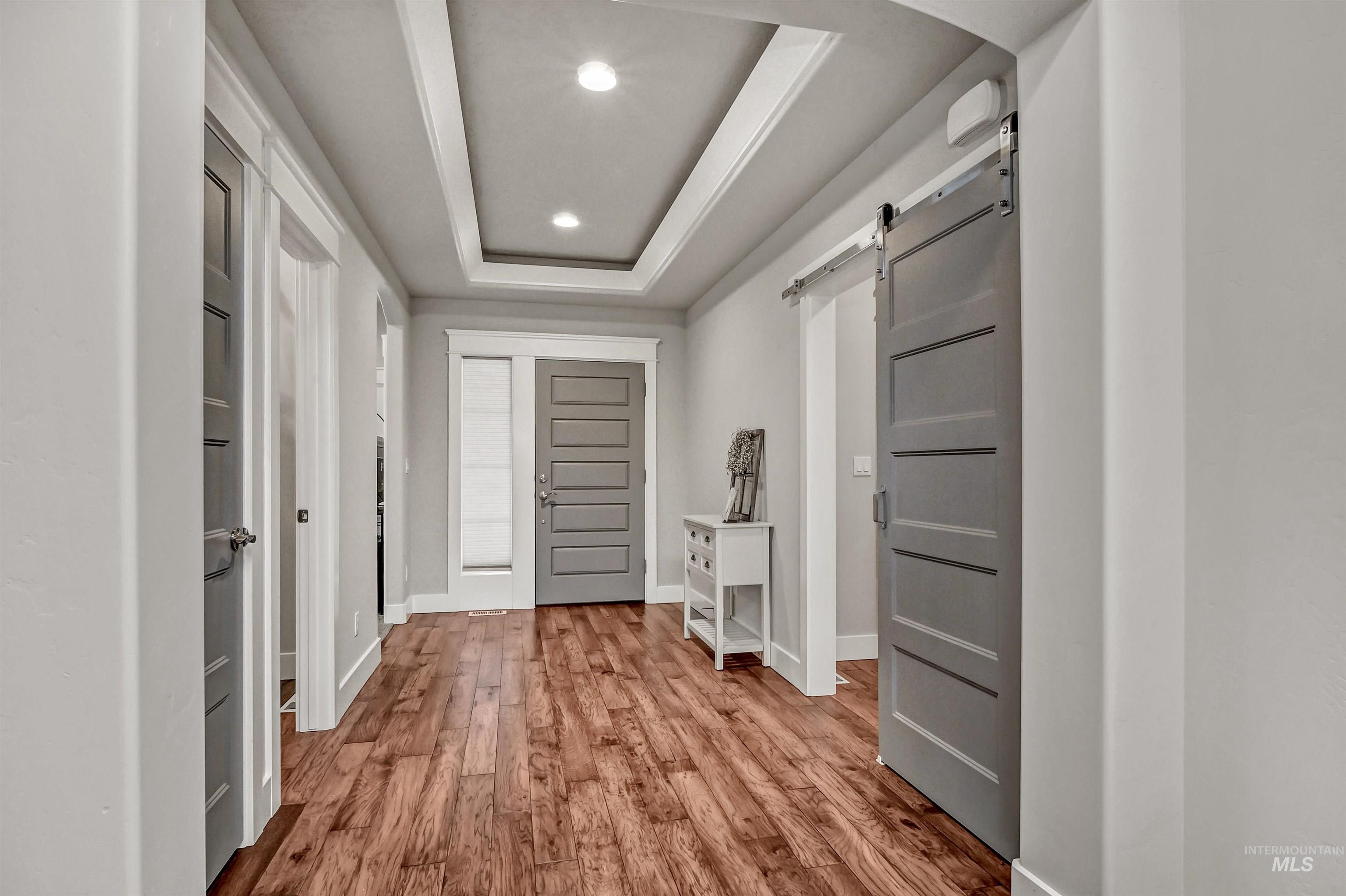 Large entrance foyer featuring a barn door, a raised ceiling, light engineered-wood floors, and recessed lighting