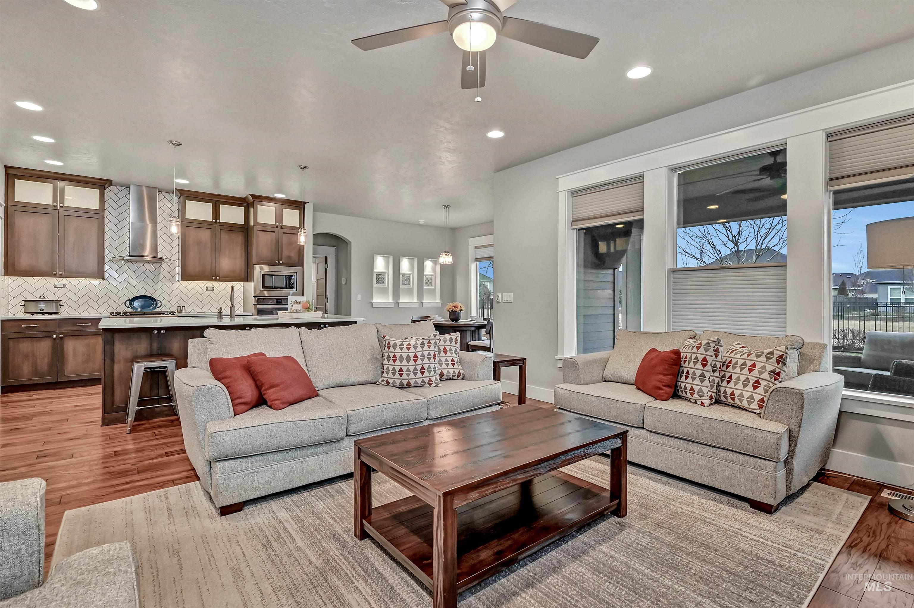 Open-style great room featuring engineered-wood flooring, a ceiling fan, a view into the kitchen & dining area, and recessed lighting
