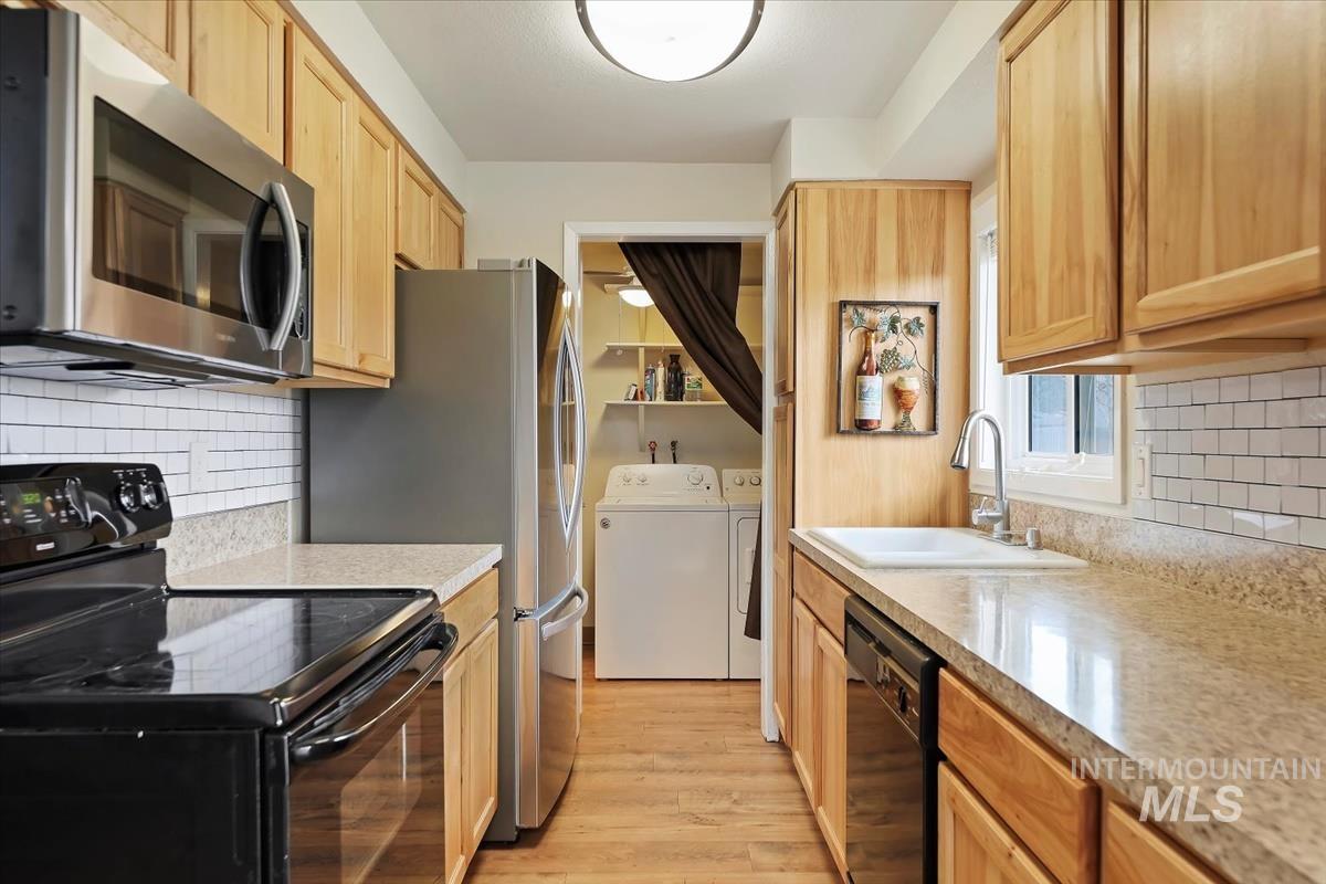 Kitchen featuring decorative backsplash, black appliances, washer and clothes dryer, light wood-style floors, and light brown cabinetry