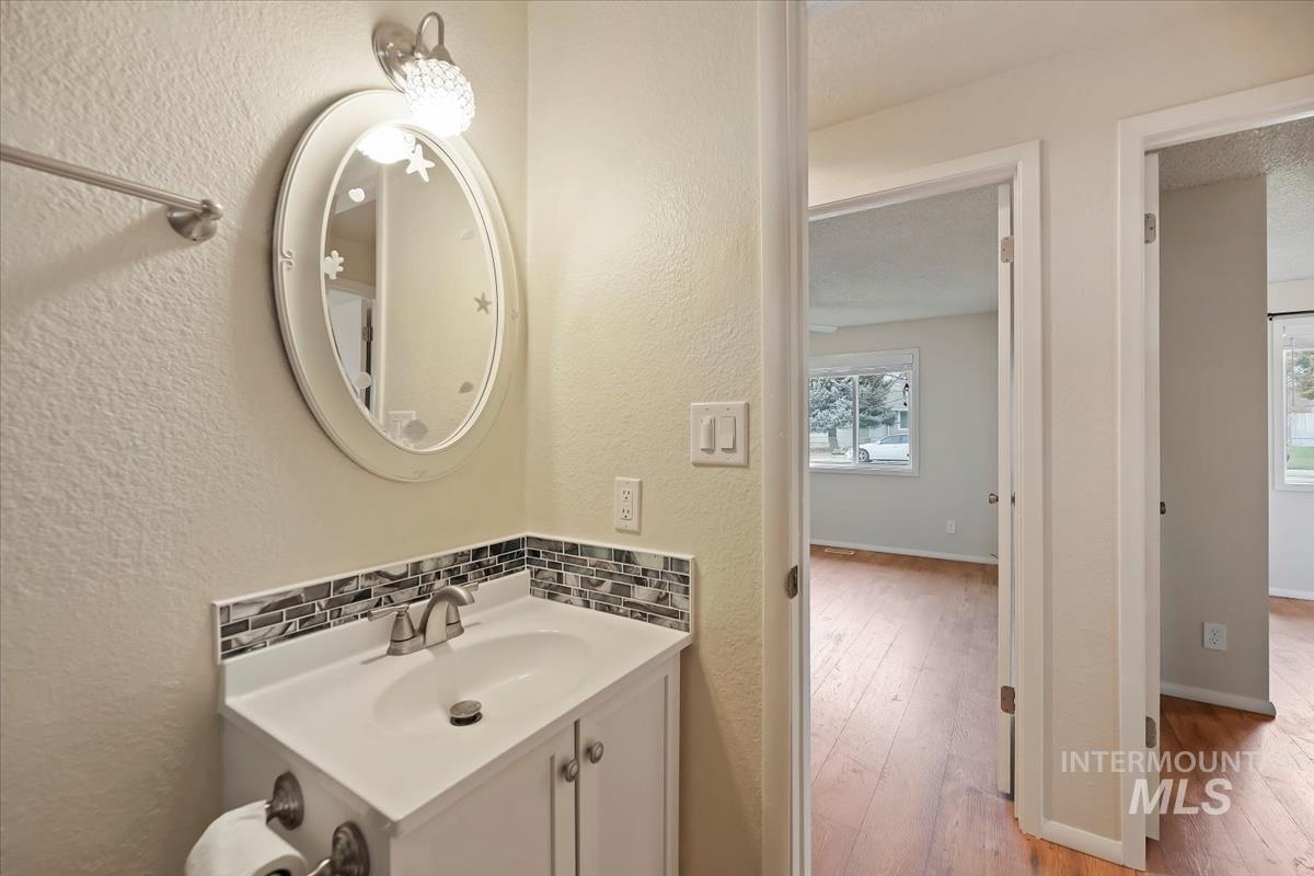 Half bath with a textured wall, decorative backsplash, vanity, and light wood-style floors