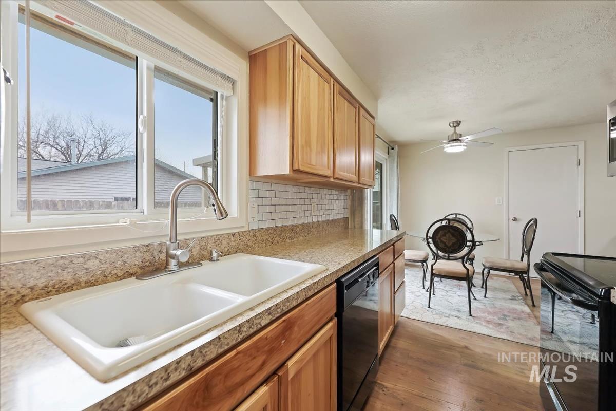 Kitchen with tasteful backsplash, black appliances, dark wood finished floors, a ceiling fan, and brown cabinets