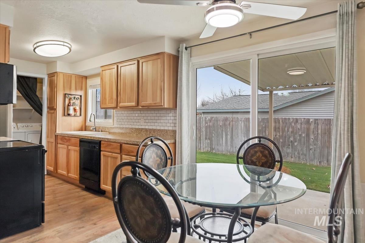 Kitchen featuring light countertops, light wood finished floors, decorative backsplash, black appliances, and washing machine and dryer