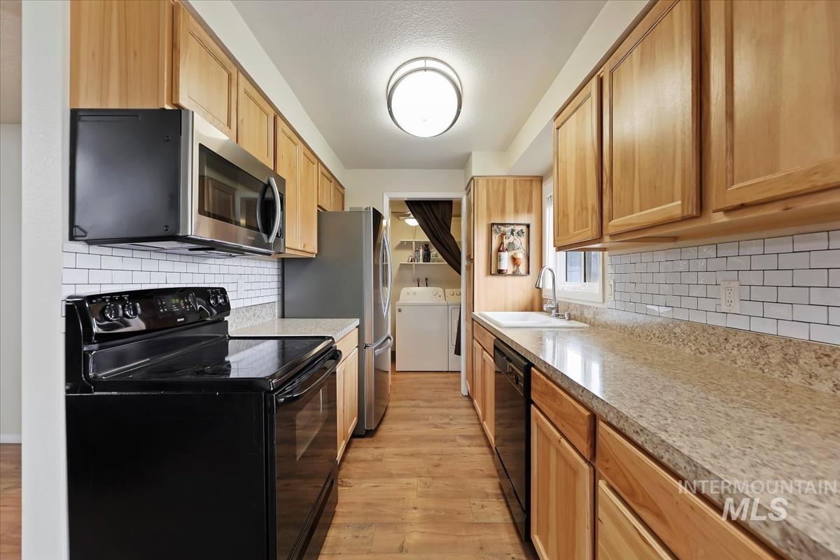 Kitchen with black appliances, washing machine and dryer, light wood-type flooring, and backsplash