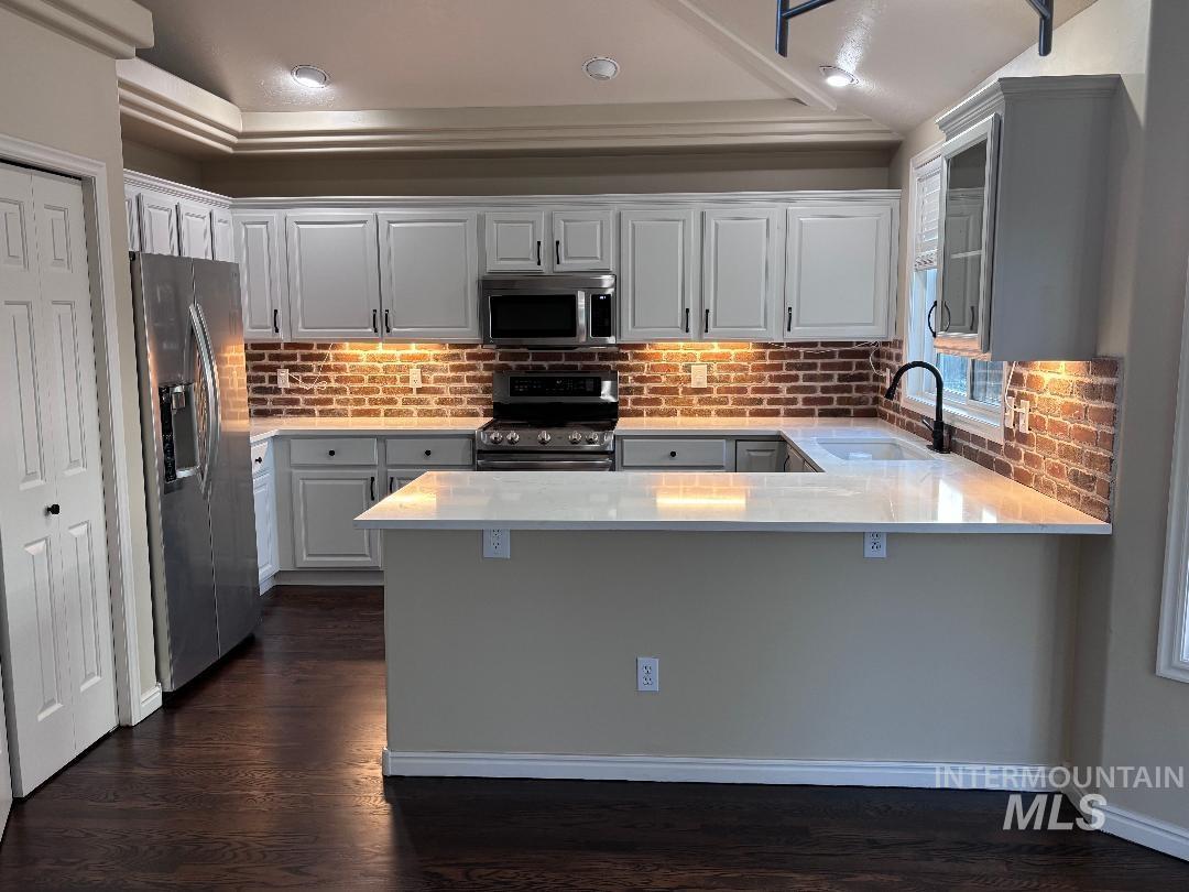 Kitchen featuring stainless steel appliances, a peninsula, light stone counters, and white cabinetry